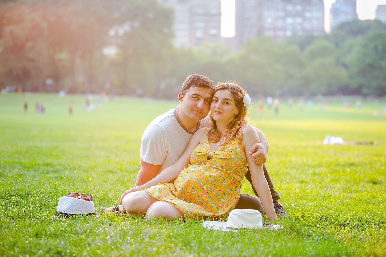 Couple enjoying sunny afternoon on grassy field with cityscape background.