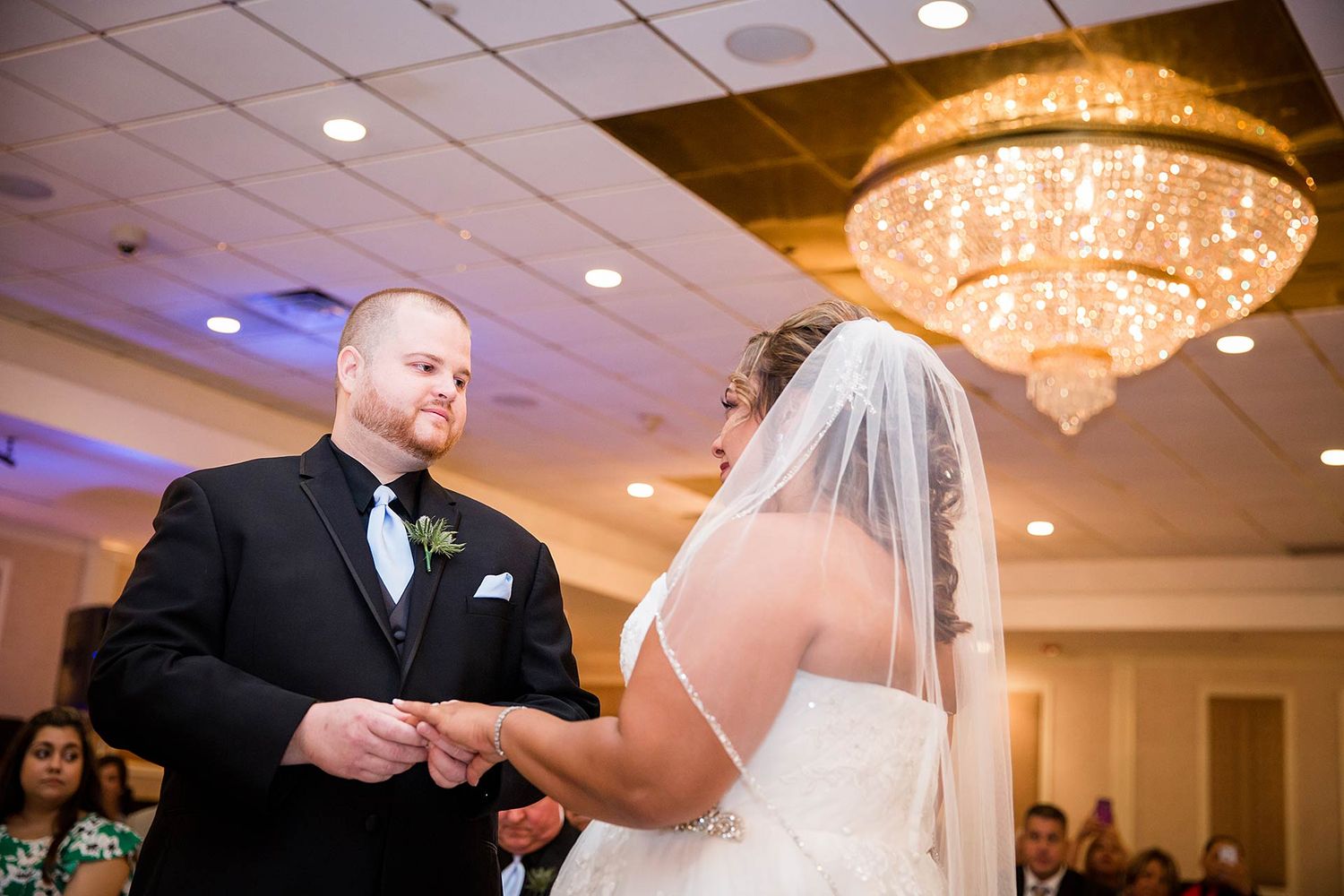 Exchange of rings during indoor wedding ceremony under crystal chandelier.