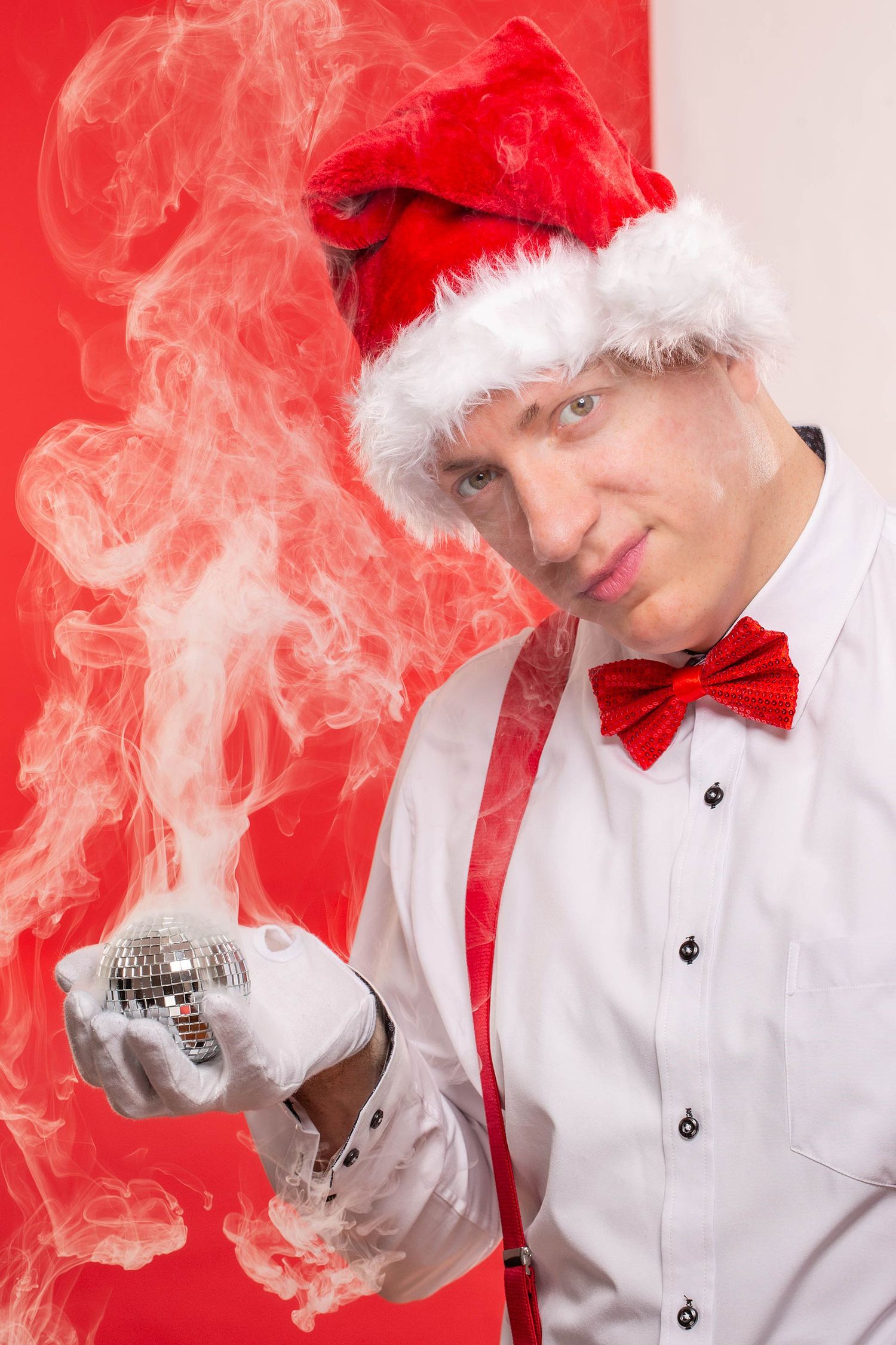 Holiday portrait with smoke effects featuring white gloves and Santa hat against red backdrop.