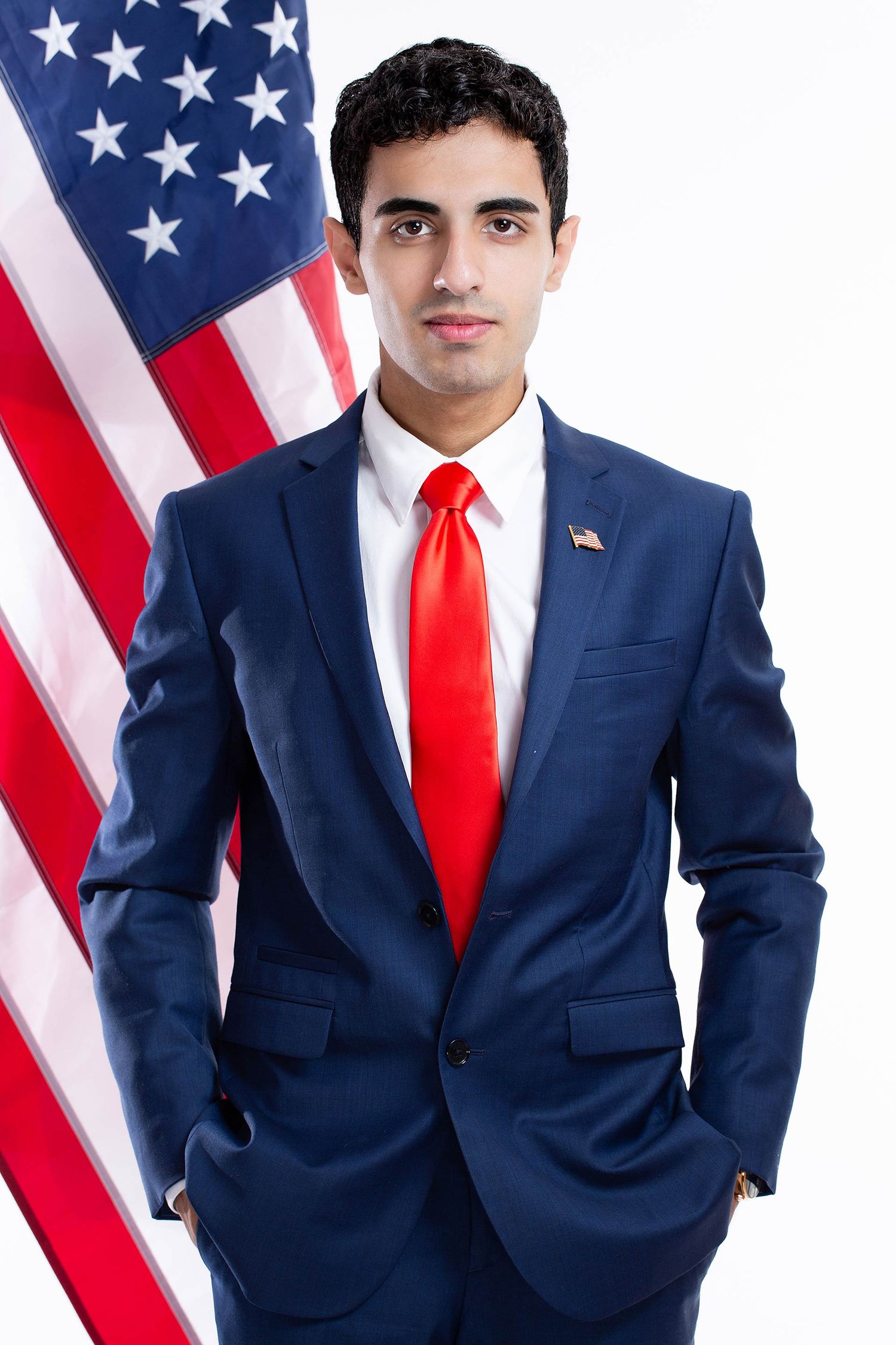 Professional in navy suit and red tie poses for series of photos with American flag backdrop.
