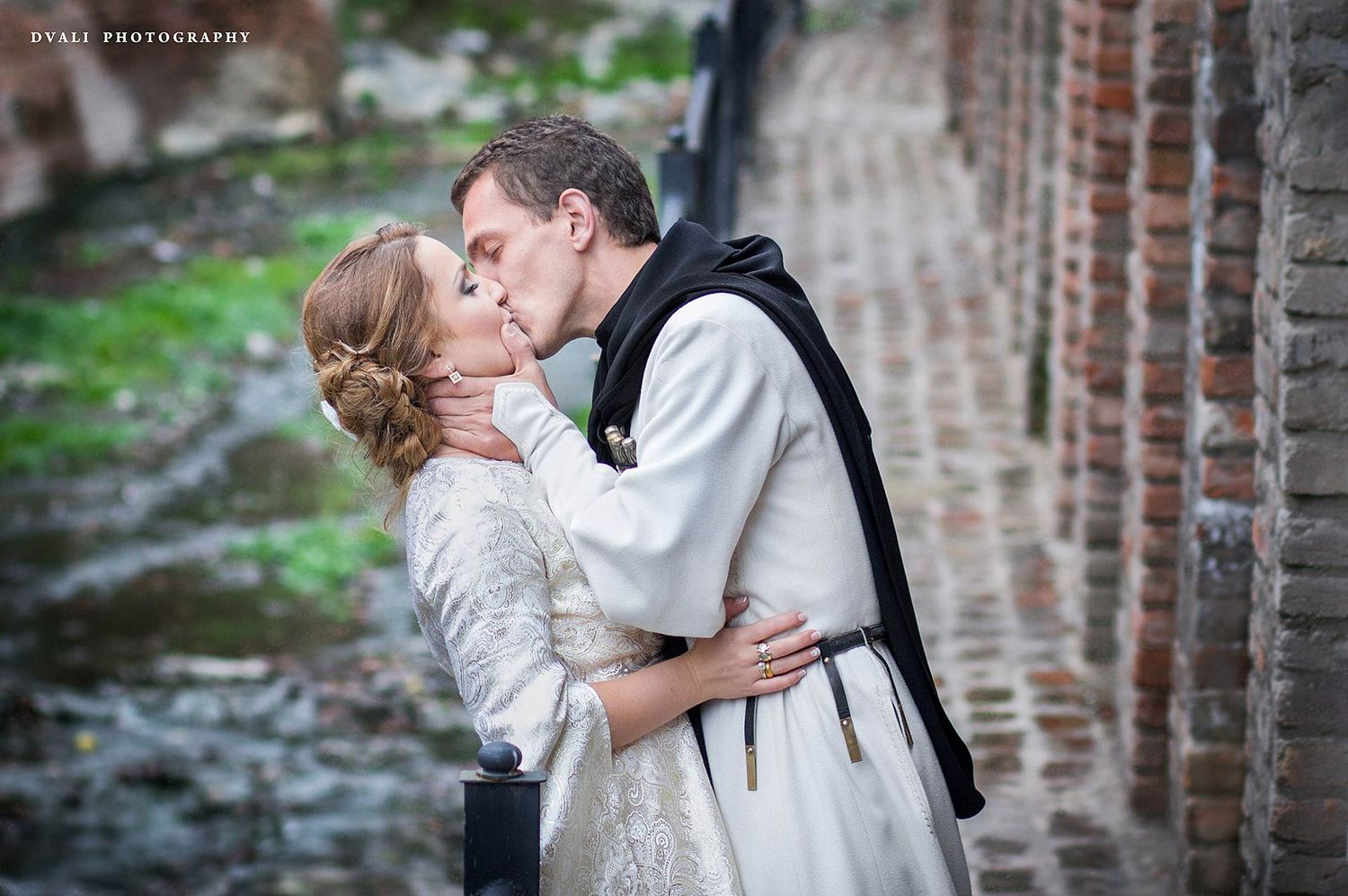 A tender moment between a couple in medieval costumes against a brick wall.