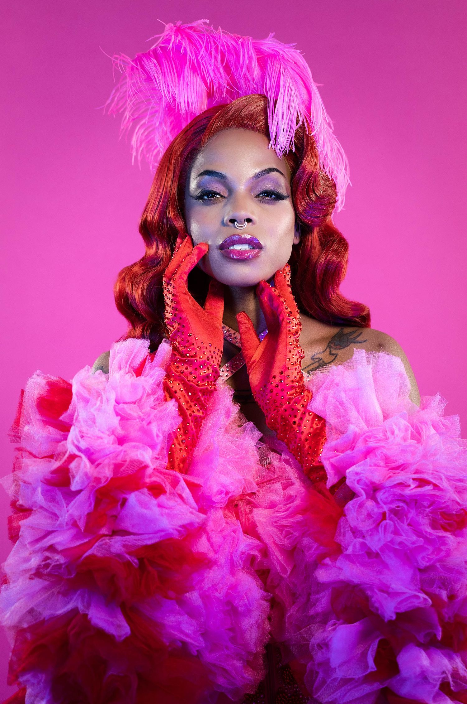 Dramatic portrait in pink ruffled dress with matching feather headpiece against magenta background.
