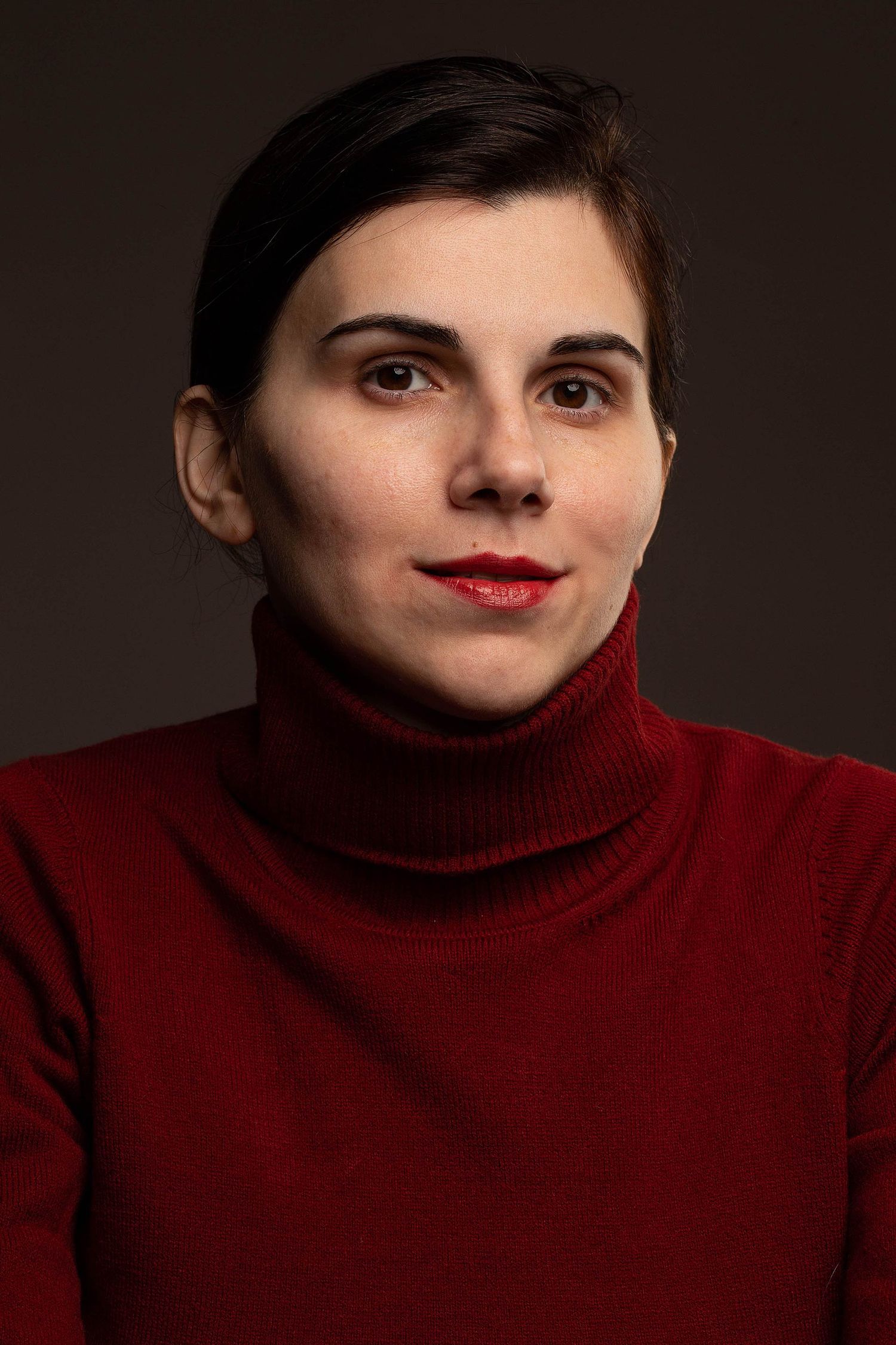 Artistic portrait featuring person in red turtleneck sweater against dark background.