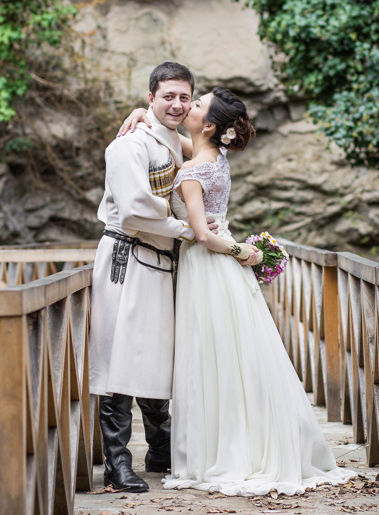 A romantic couple poses on wooden stairs surrounded by natural stone walls.