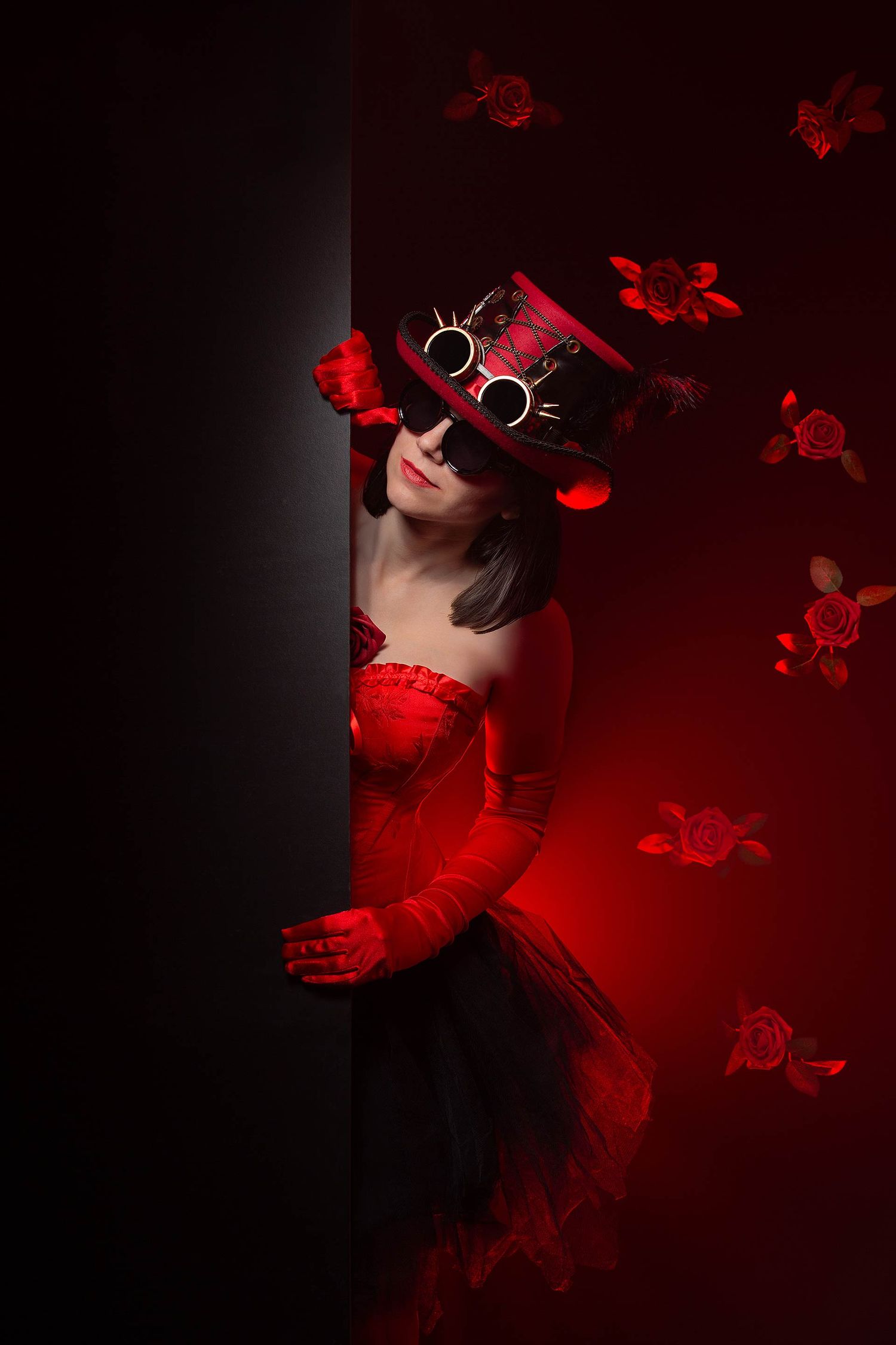Artistic portrait with figure in steampunk hat peeking from behind dark wall with red lighting.