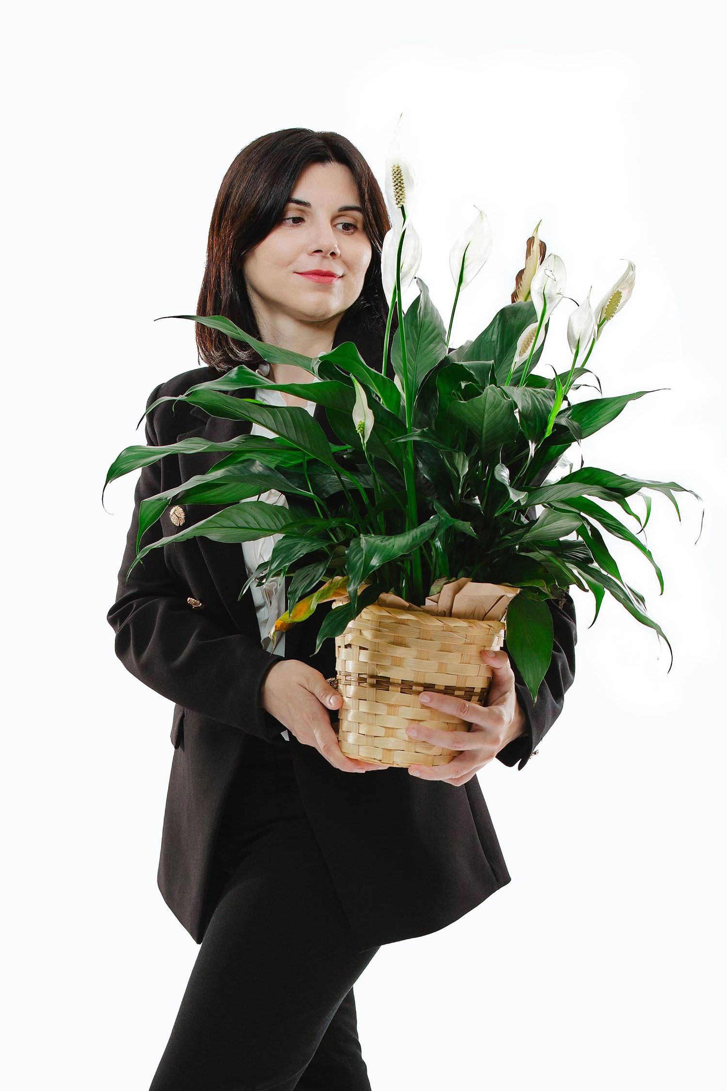 Person in black outfit holding potted peace lily plant against white background.