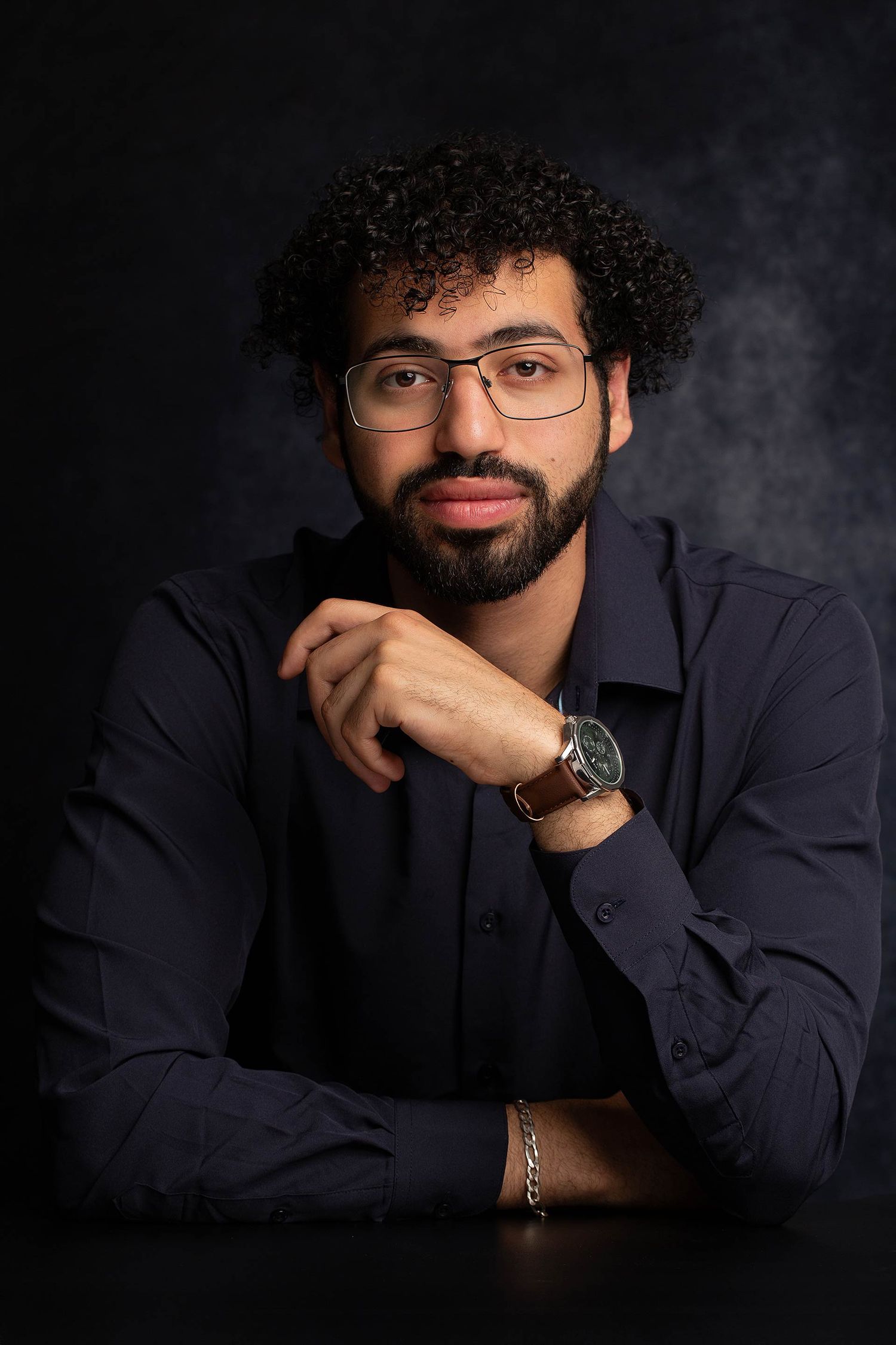 Professional headshots with moody lighting showing casual poses against dark backdrop.