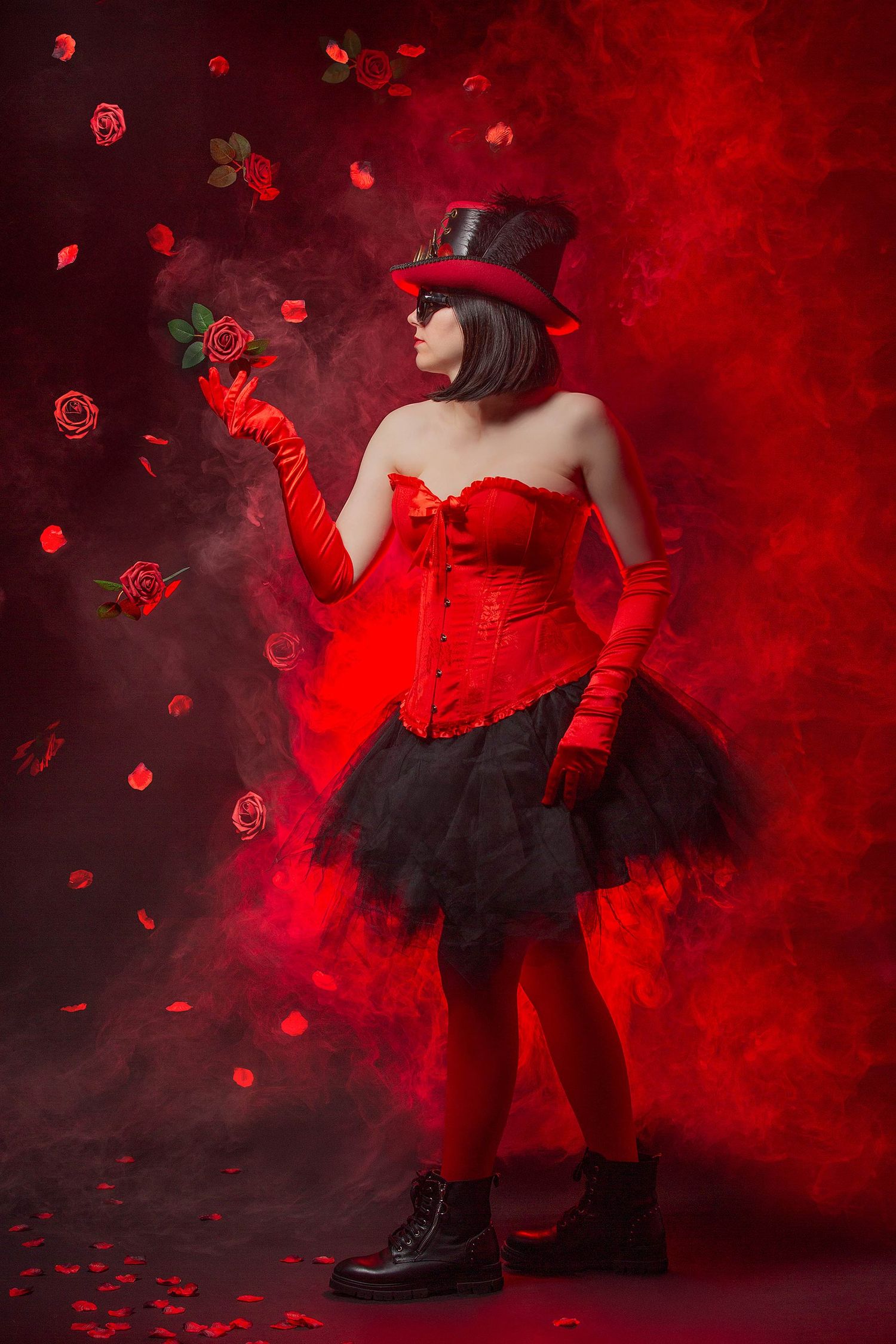 Gothic performer in red corset and top hat with rose amid floating red petals and smoke.