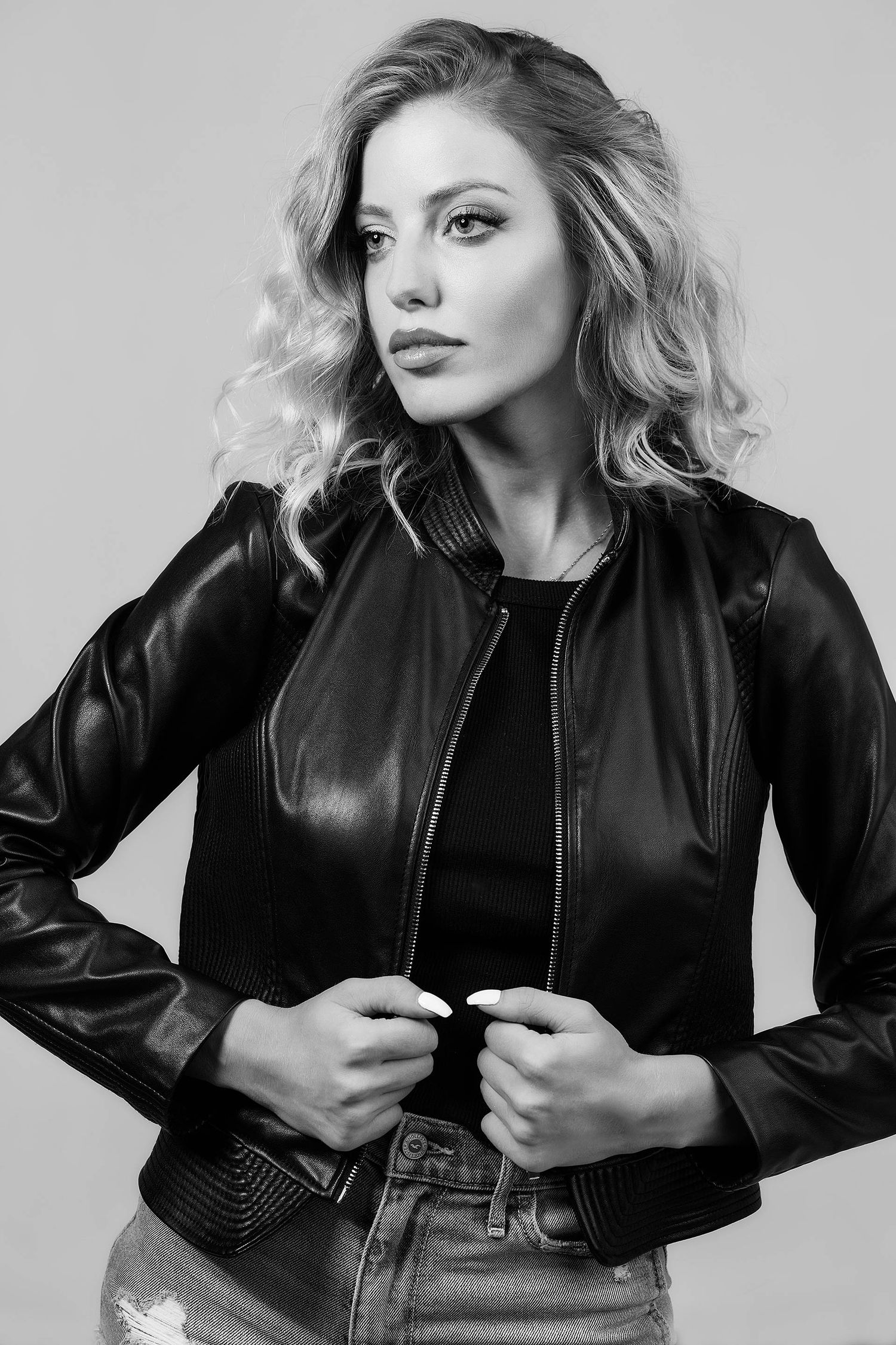 Fashion model in black leather jacket poses in black and white studio photoshoot.
