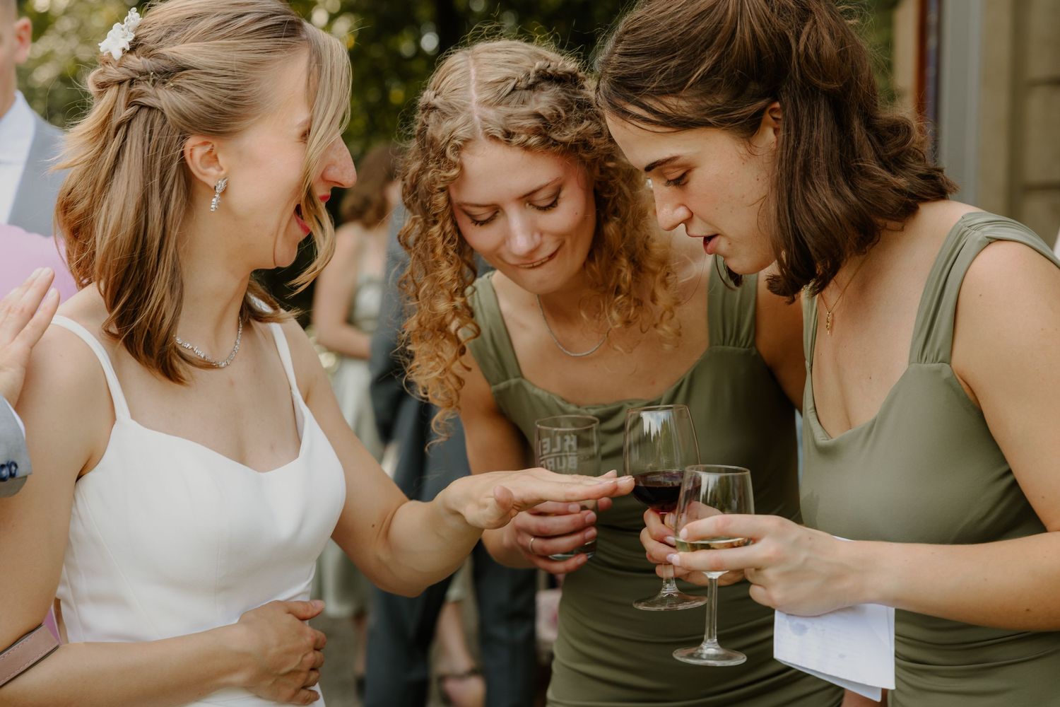 Twee bruidsmeisjes kijken vol verwondering naar de gloednieuwe trouwring van hun beste vriendin de bruid.