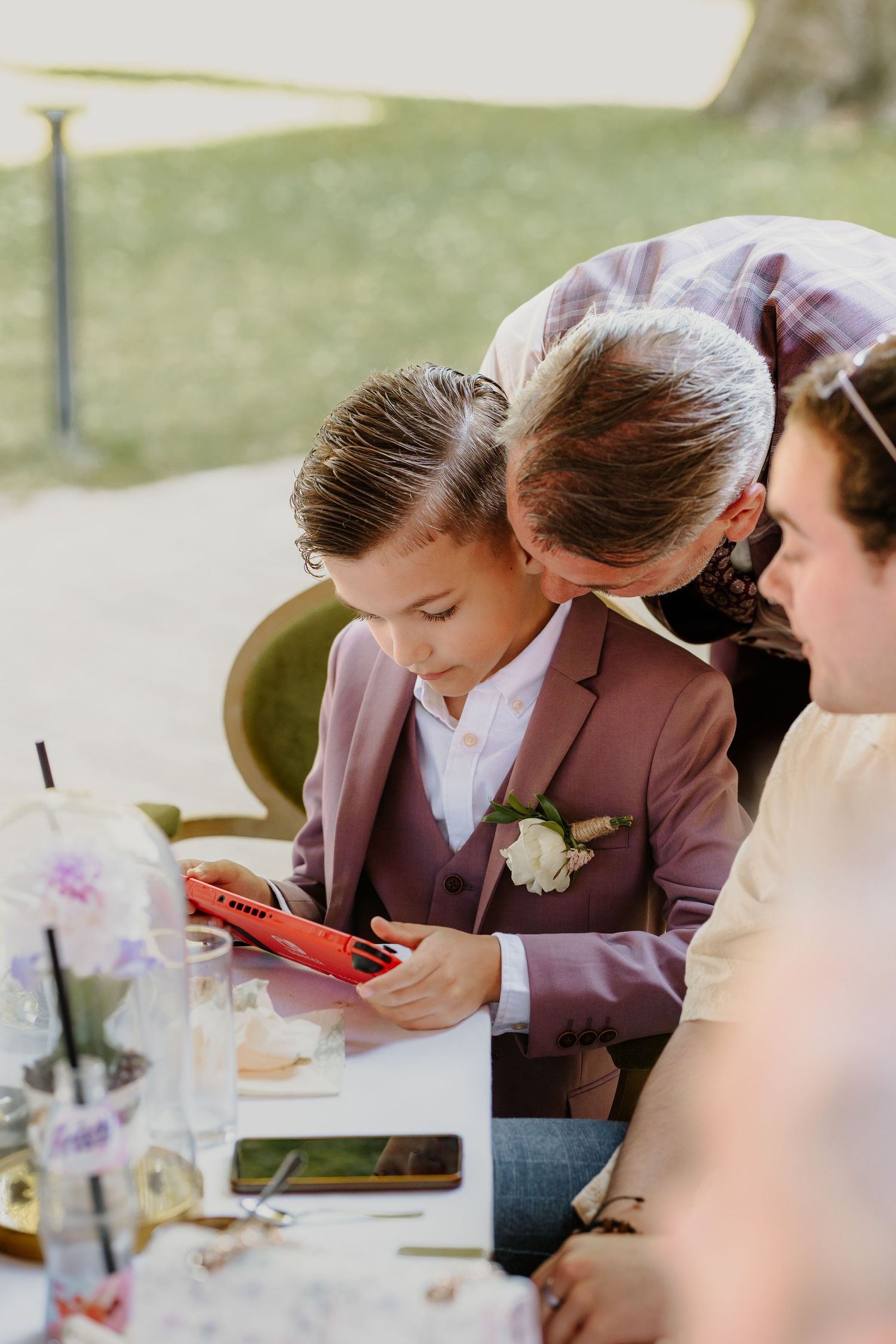 Een bruidsjonker speelt op zijn Nintendo Switch terwijl zijn vader hem een knuffel geeft.