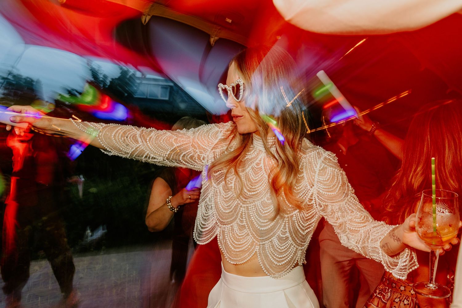 Bruid danst met zonnebril en glas in haar hand tijdens het trouwfeest