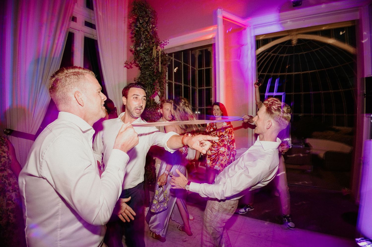 Gasten dansen de Limbo op een kleurrijk verlichte dansvloer tijdens het trouwfeest.