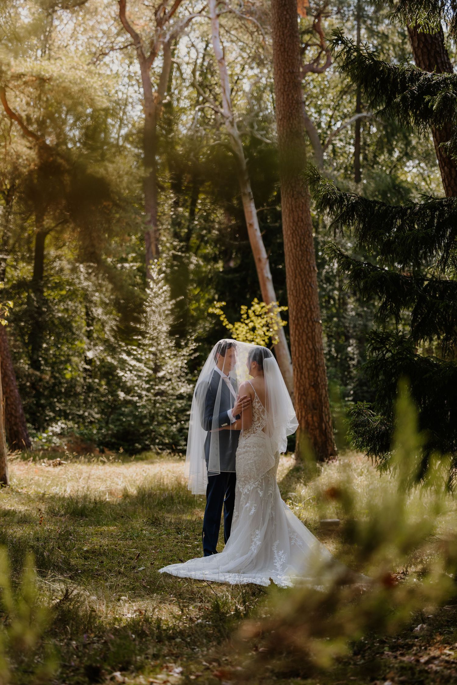 Een bruidspaar maakt foto's onder de sluier van de bruid in de Heidetuin in Driebergen