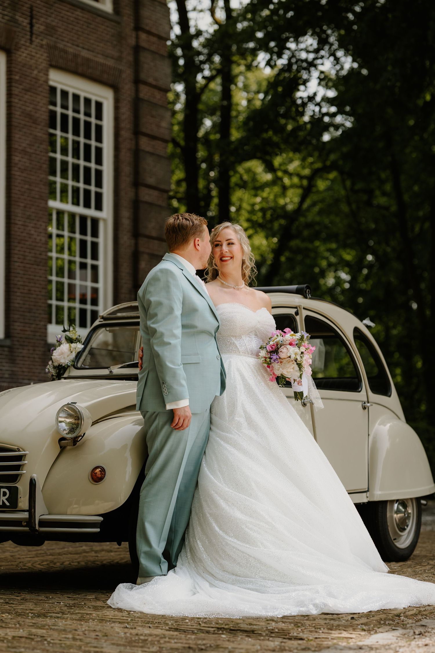 Bruidspaar poseert voor hun trouwauto bij Buitenplaats Sparrendaal