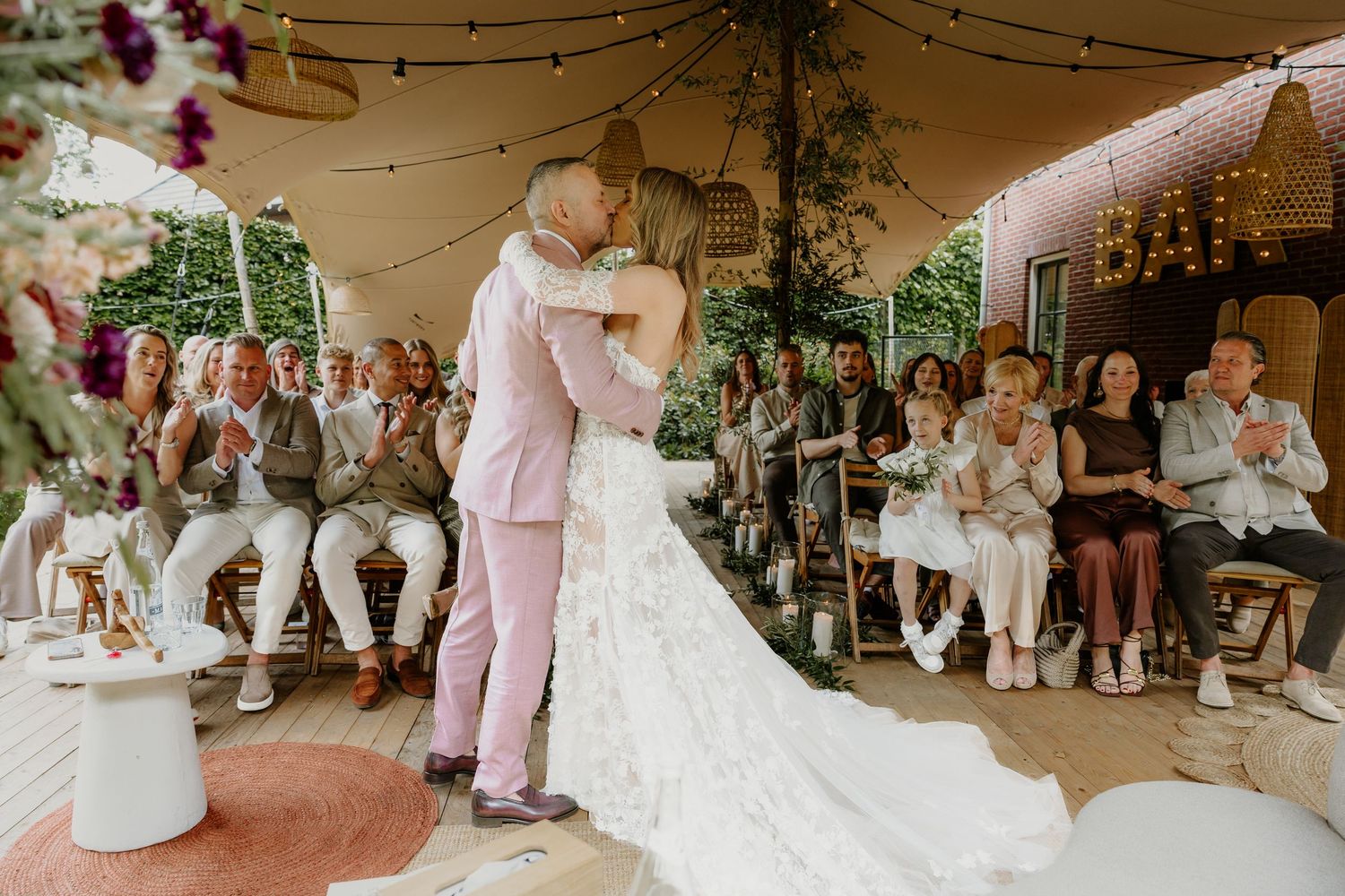 Bruidspaar kust elkaar tijdens de ceremonie terwijl familie en vrienden toekijken