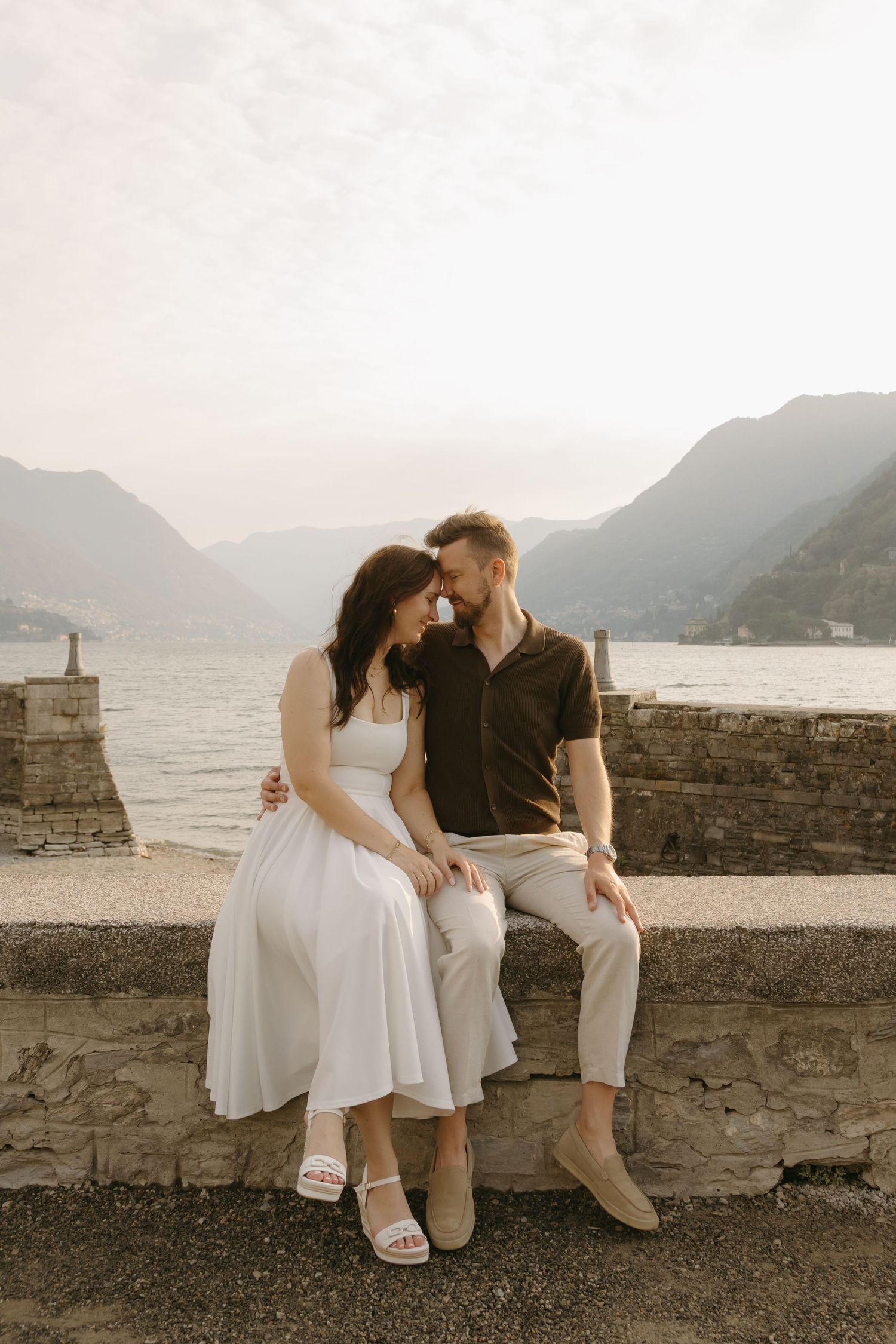 Trouwfotografen Lisa en André zitten samen op een muurtje met achter hun uitzicht op het prachtige meer Como in Italië.