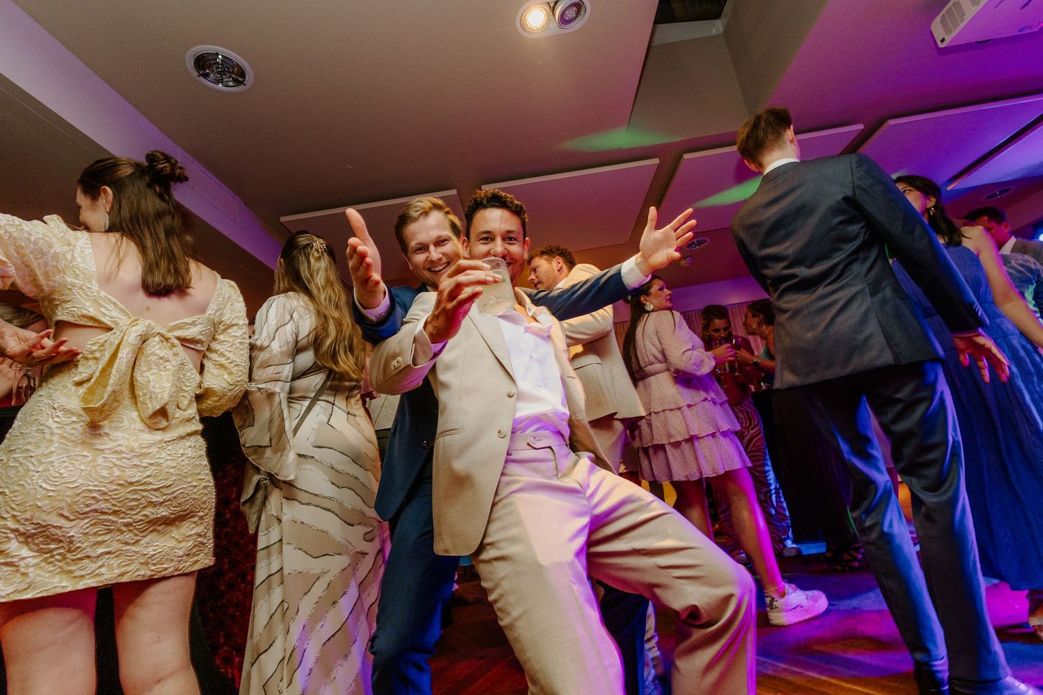 Feestende gasten op de dansvloer tijdens een sfeervol verlicht trouwfeest.