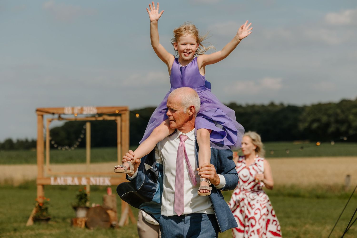 een bruidsmeisje zwaait vrolijk vanaf de schouders van haar opa.