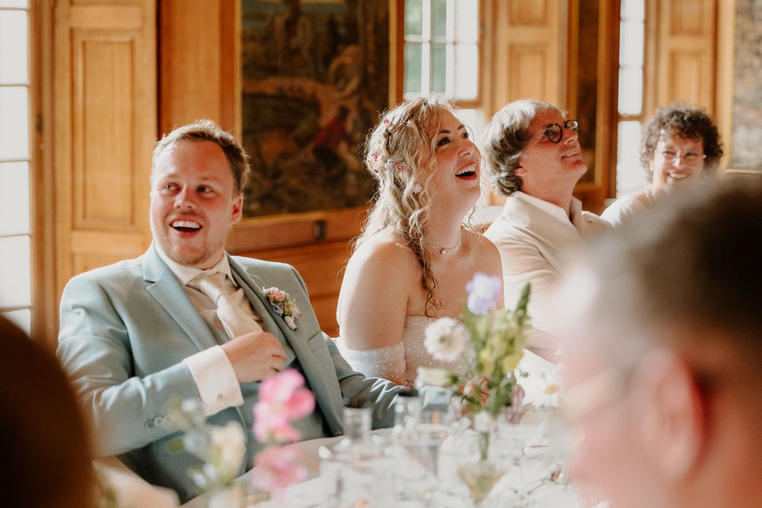 Bruidspaar lacht samen tijdens de speeches bij het bruiloftsdiner