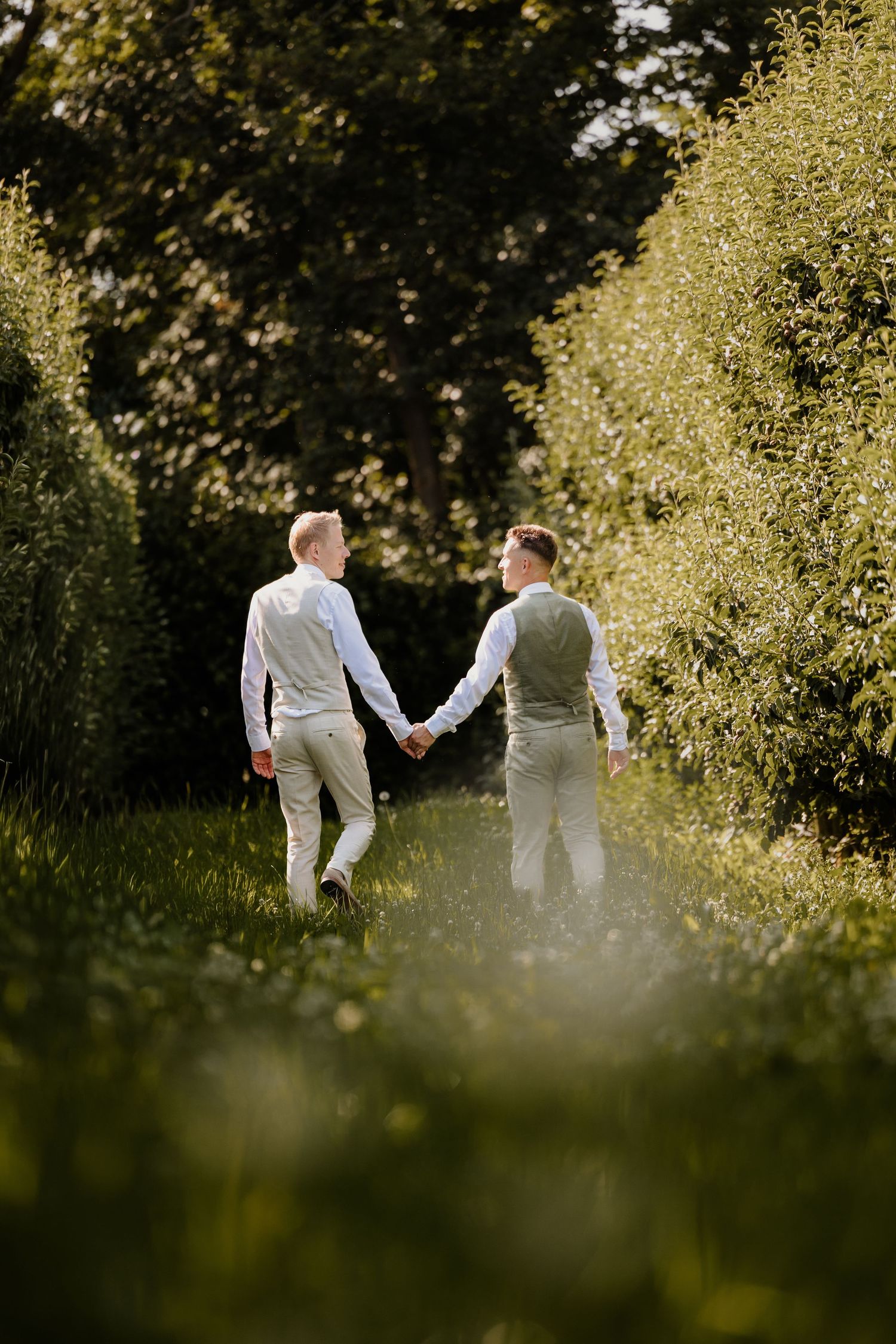 Twee mannen tijdens hun bruiloft lopen hand in hand door de boomgaard