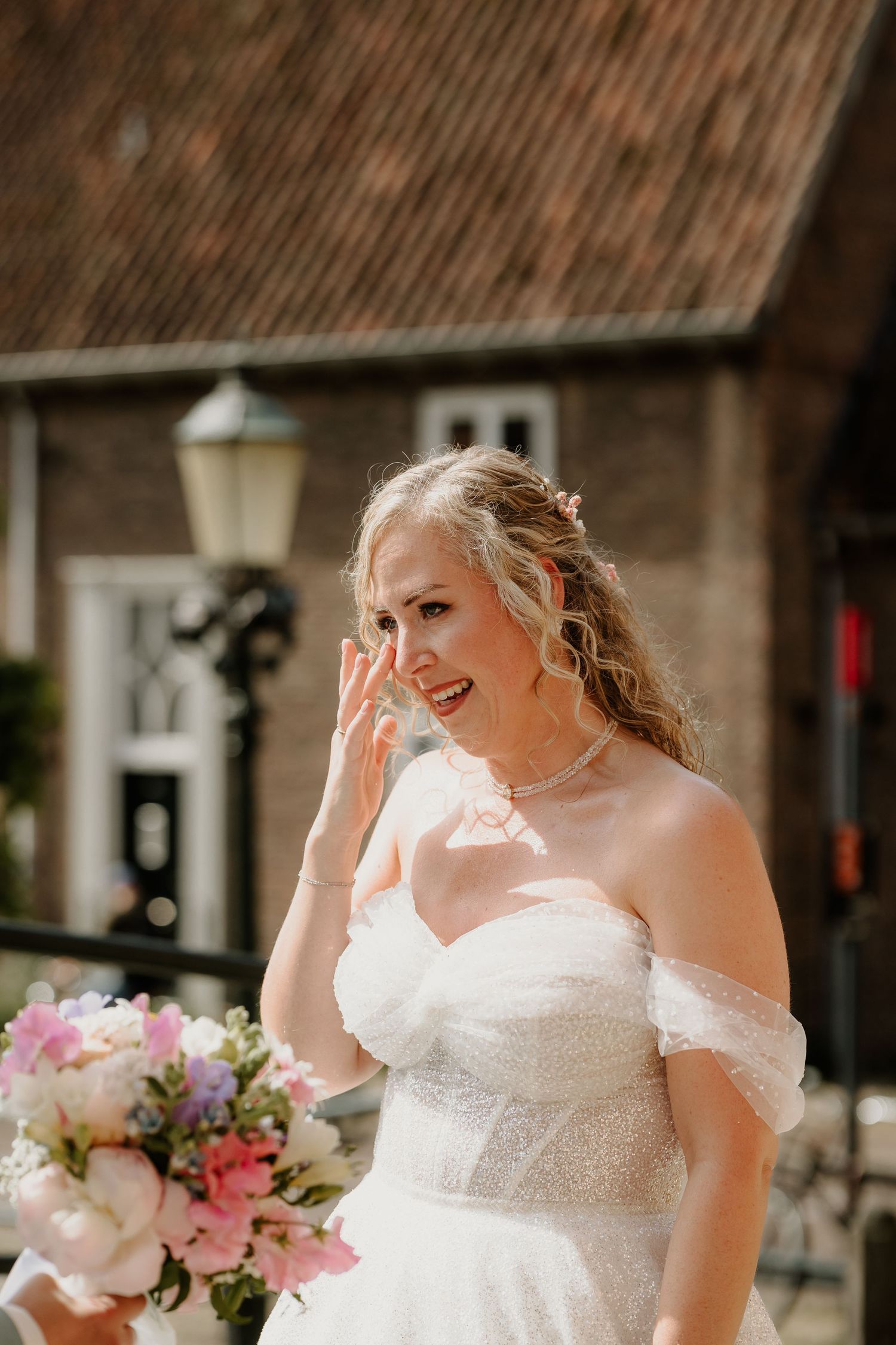 Geëmotioneerde bruid met bruidsboeket in het zonlicht op tijdens de first look op hun trouwdag