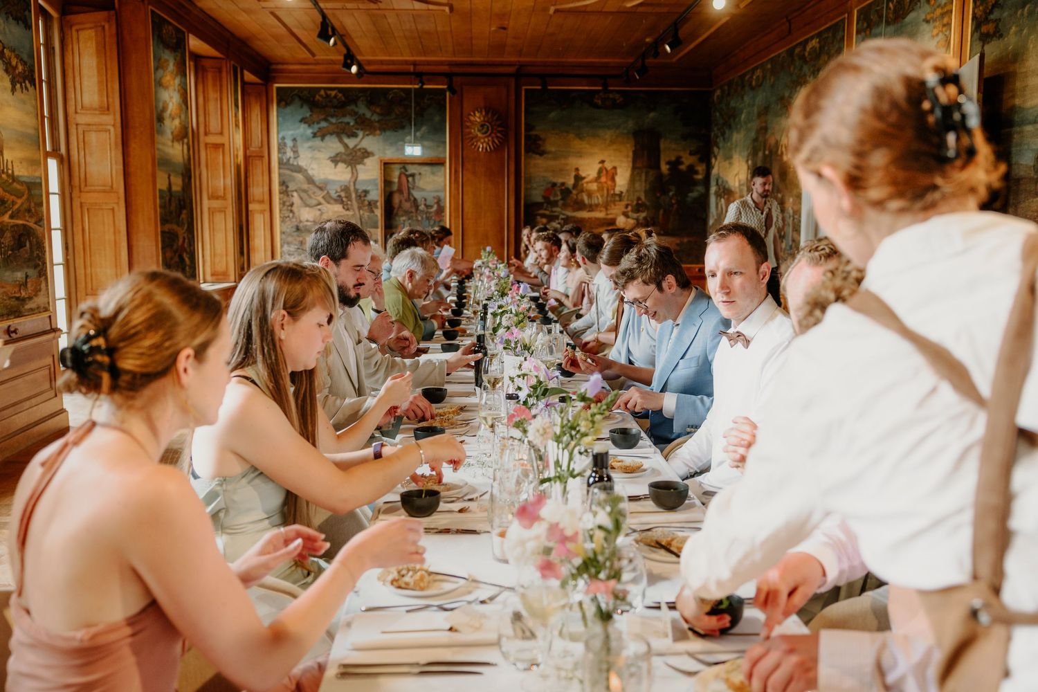 Bruidspaar en gasten samen aan een lange gedekte tafel tijdens het diner