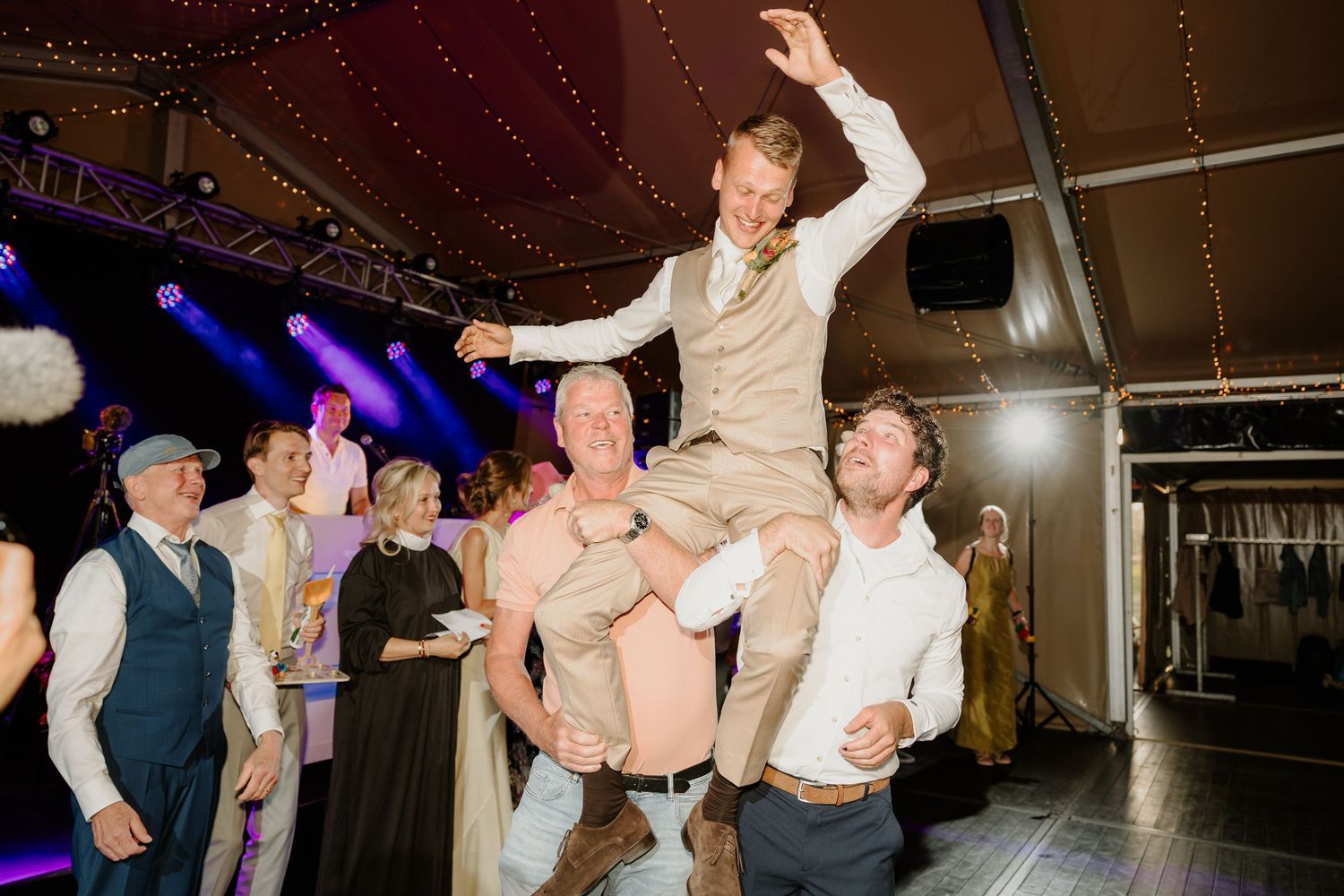 Bruidegom wordt door zijn vrienden opgetild tijdens het trouwfeest