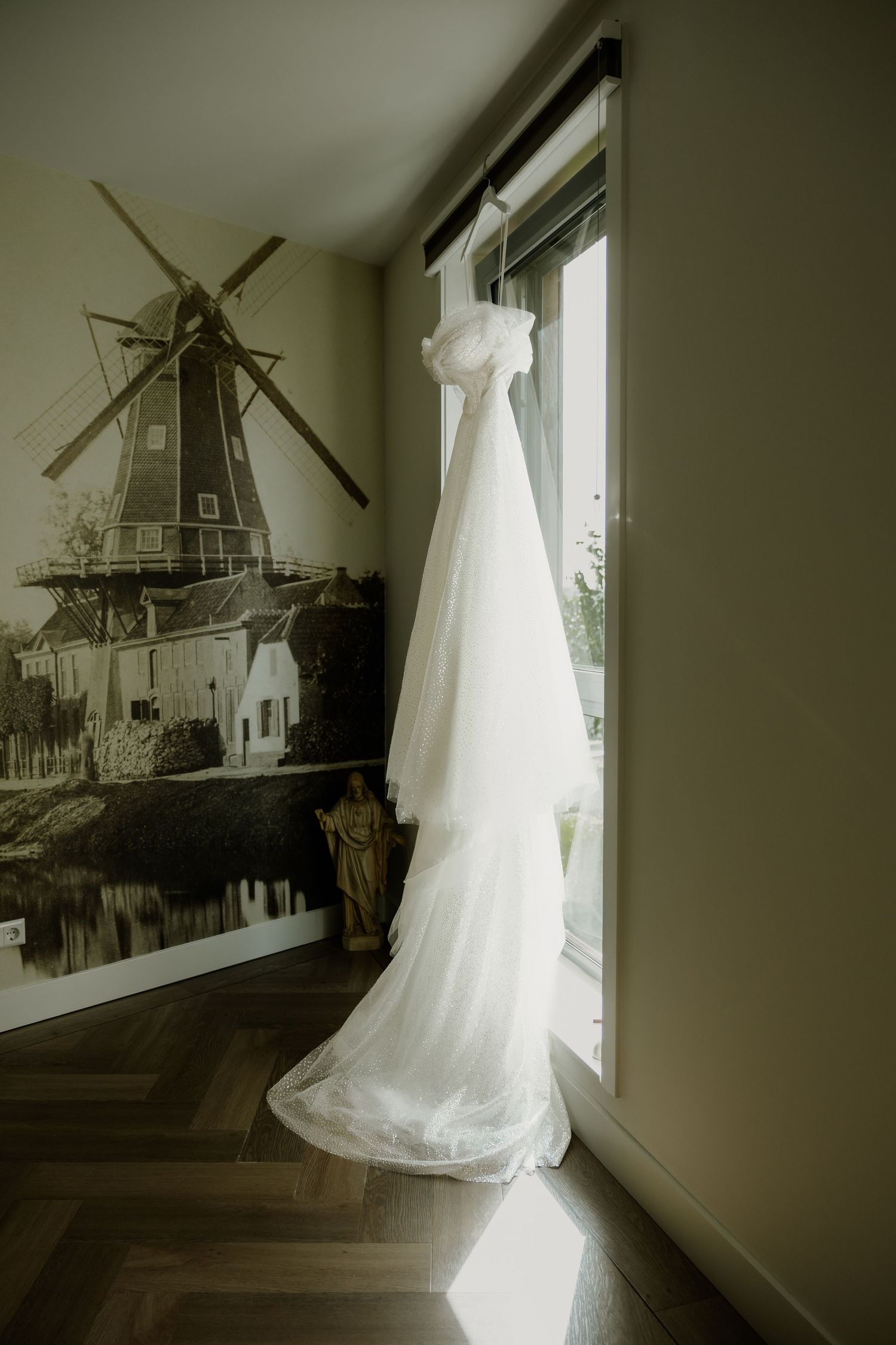 Trouwjurk hangt klaar bij het raam tijdens de voorbereidingen van de bruid