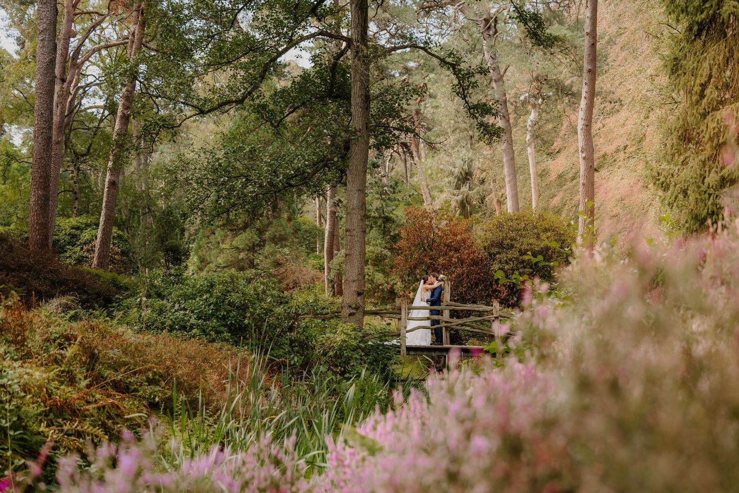 Een bruidspaar staat op een brug in de weelderige Heidetuin in Driebergen