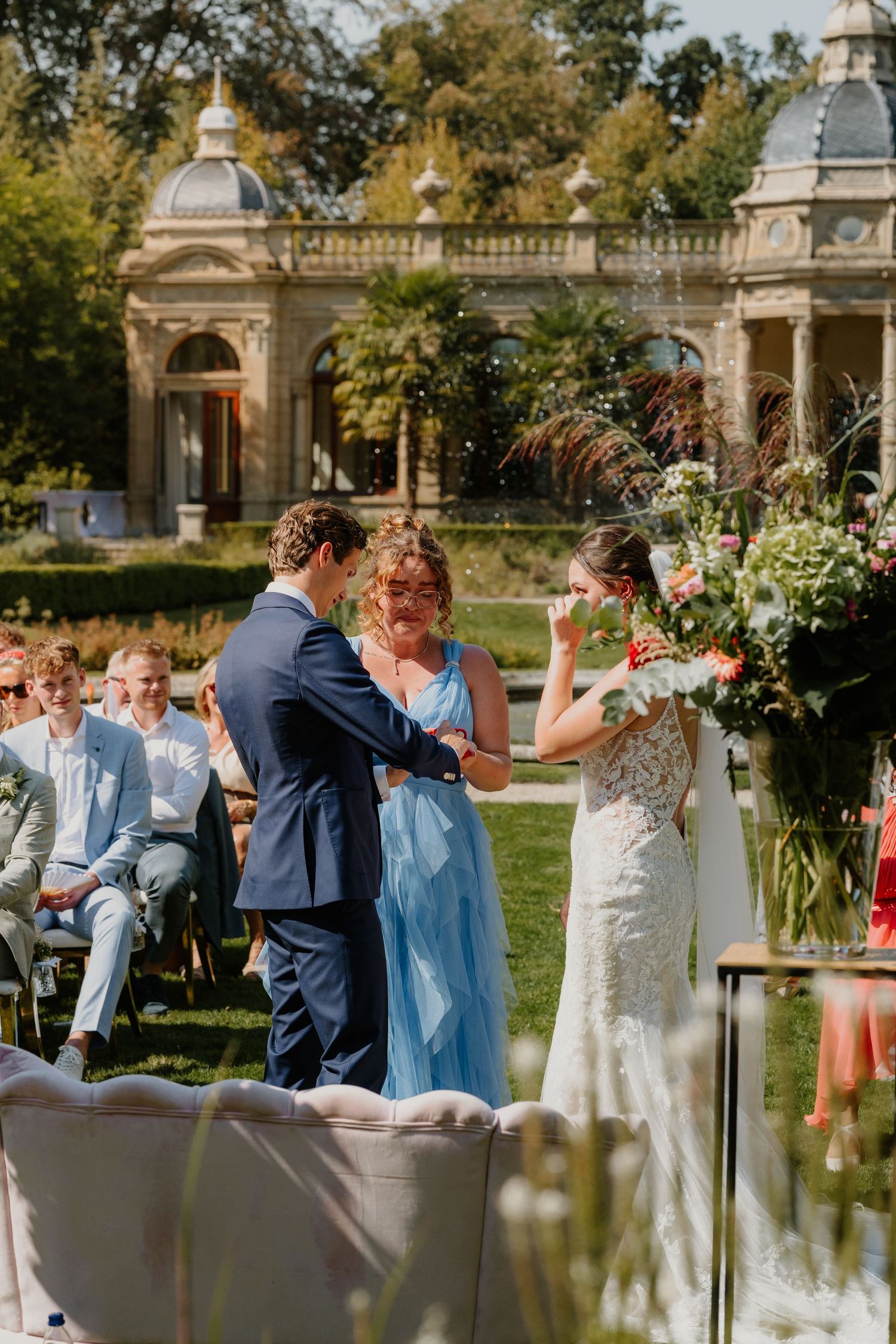 Bruidspaar wisselt de ringen uit tijdens een buitenceremonie in de tuin van Oranjerie Hydepark