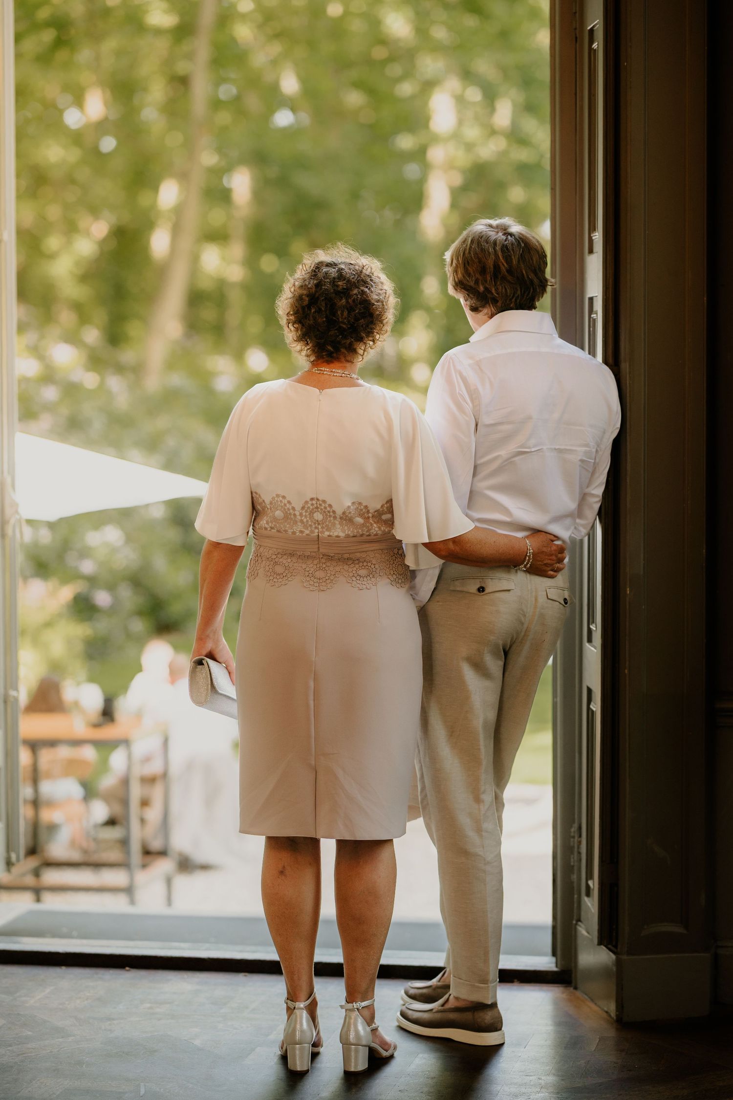 De ouders van de bruid staan vol trots te kijken naar alle activiteiten buiten op de bruiloft.