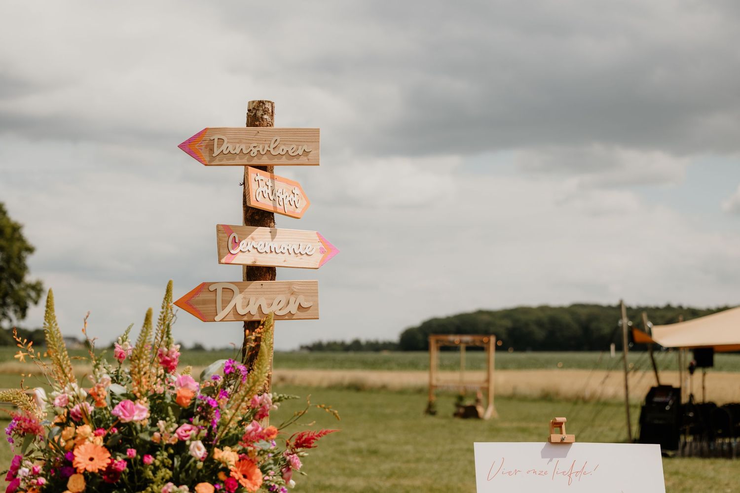 Wegwijzer tussen kleurrijke bloemen op een buitenbruiloft