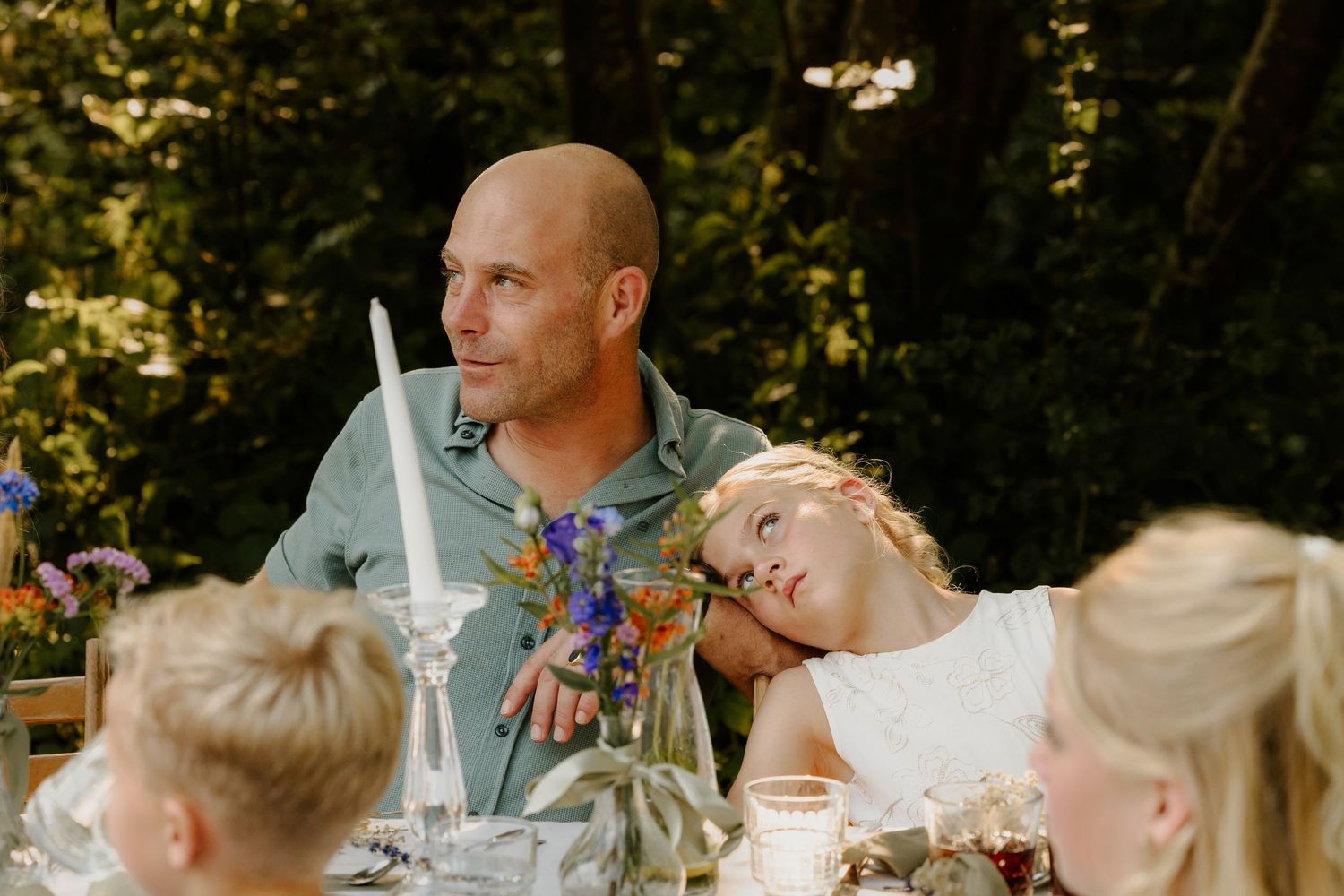 Meisje staart verveeld naar de lucht terwijl ze tegen haar vader leunt tijdens het bruiloftsdiner