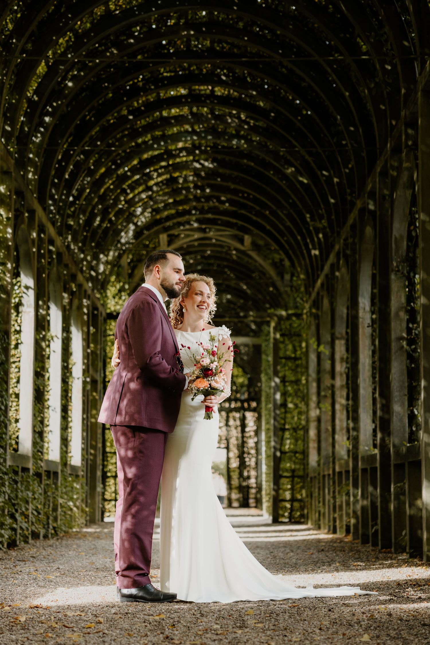 Bruidspaar omhelst elkaar onder een lange groene begroeide pergola