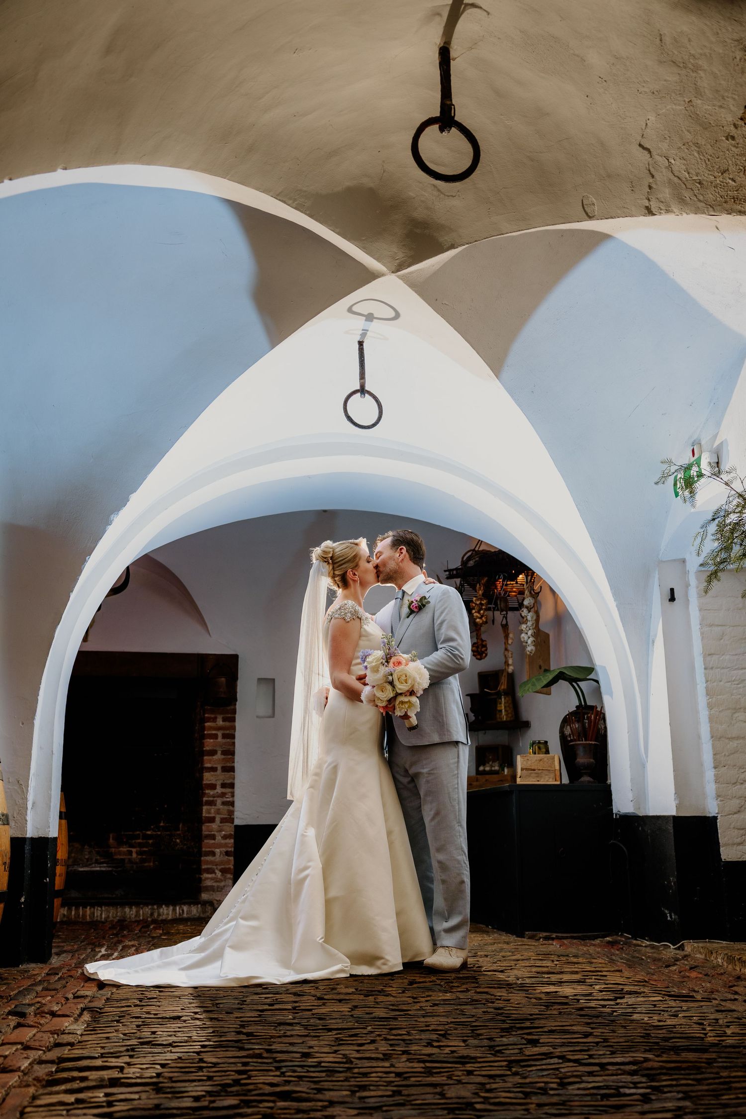 Een bruidspaar kust elkaar op een artistieke foto in de kelder van Kasteel Wijenburgh
