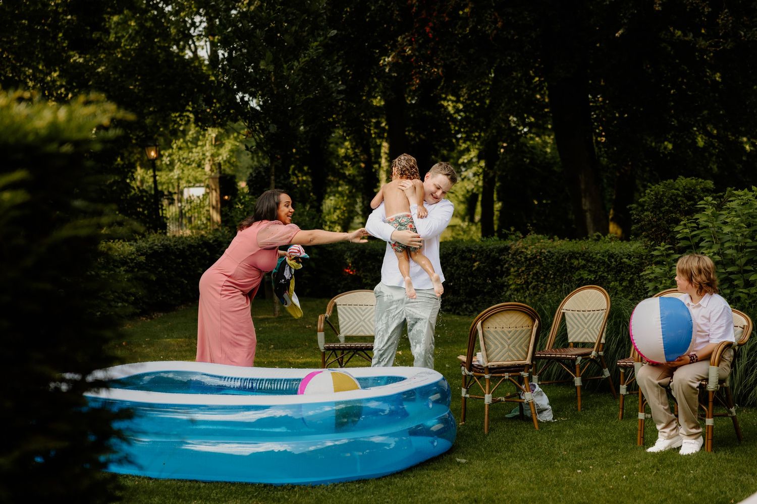 Jongetje wordt uit een opblaaszwembadje getild op een hete zomerbruiloft. Zijn moeder kijkt bezorgd naar het natte pak van de gast.