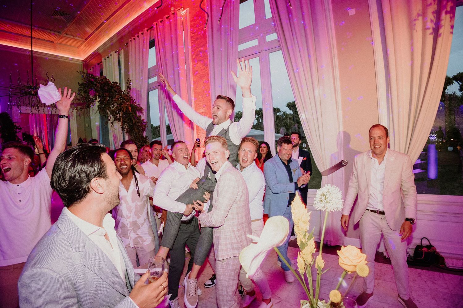 Bruidegom wordt door zijn vrienden opgetild tijdens het trouwfeest op de dansvloer