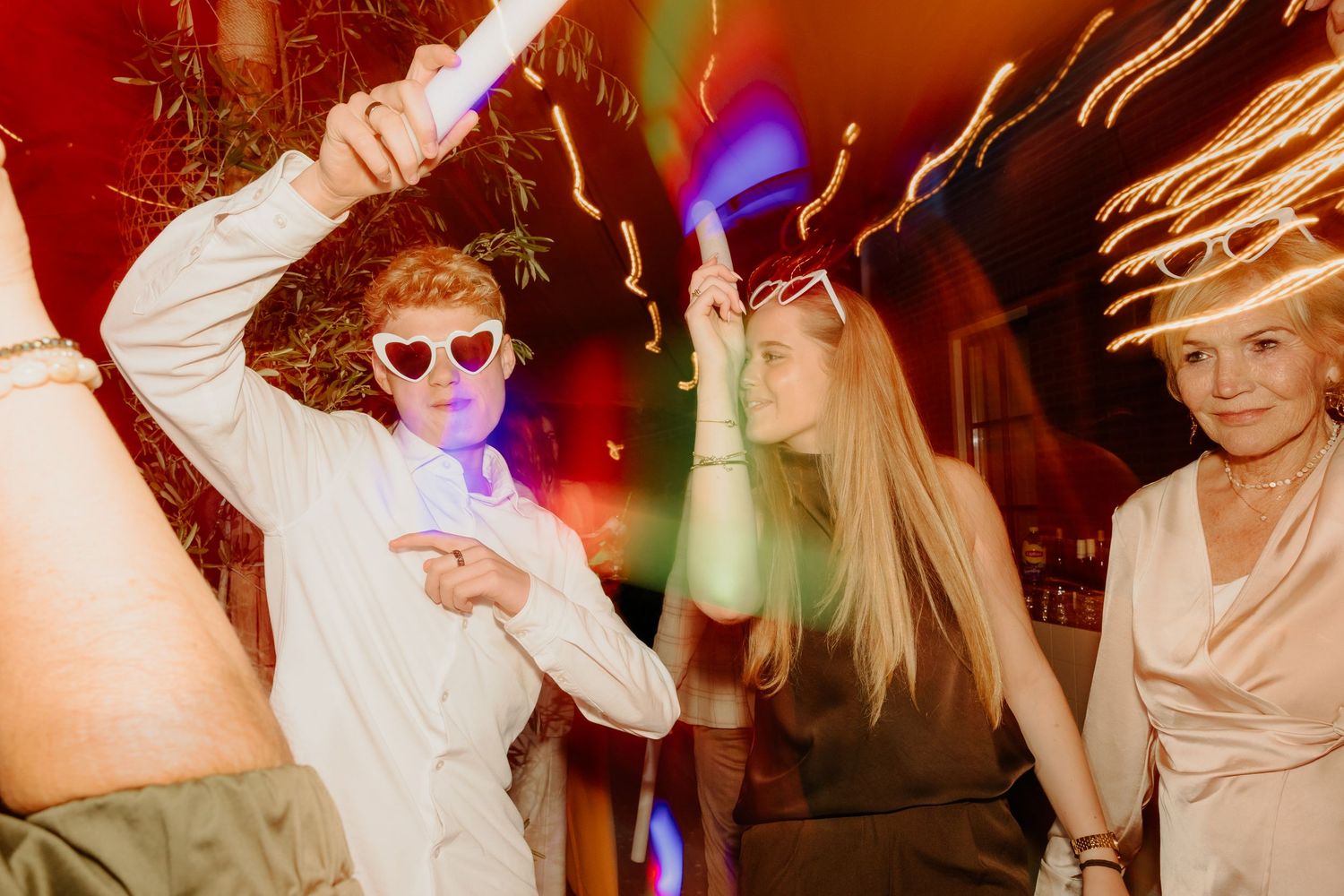Bruiloftsgasten dansen met zonnebrillen onder kleurrijke feestverlichting