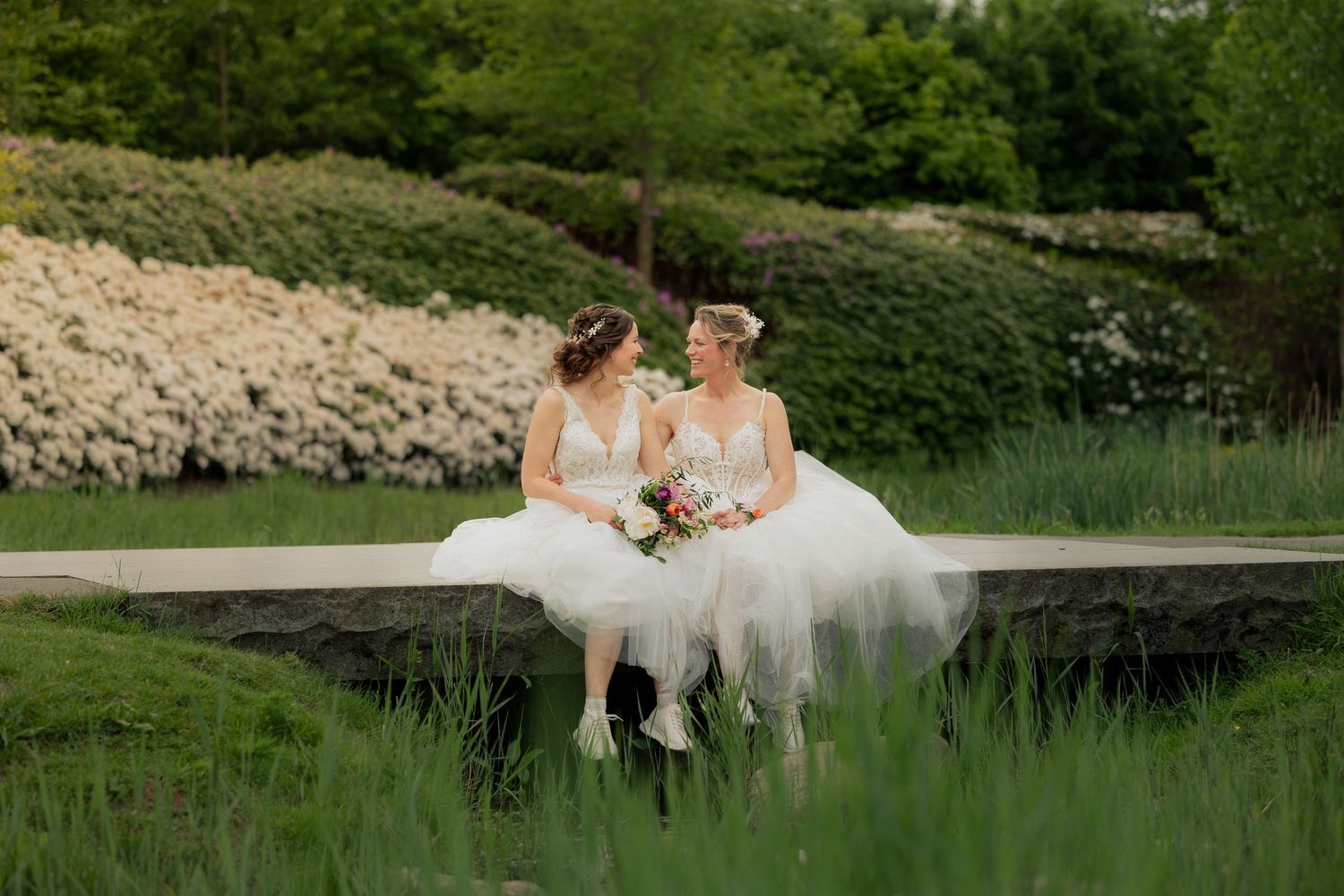 Twee bruiden in trouwjurken tijdens een romantische fotoshoot in een groene tuin