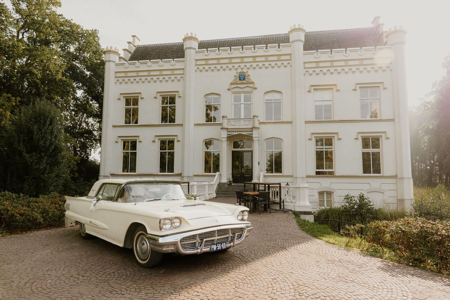 Klassieke trouwauto geparkeerd voor een statige witte trouwlocatie Huis Scherpenzeel