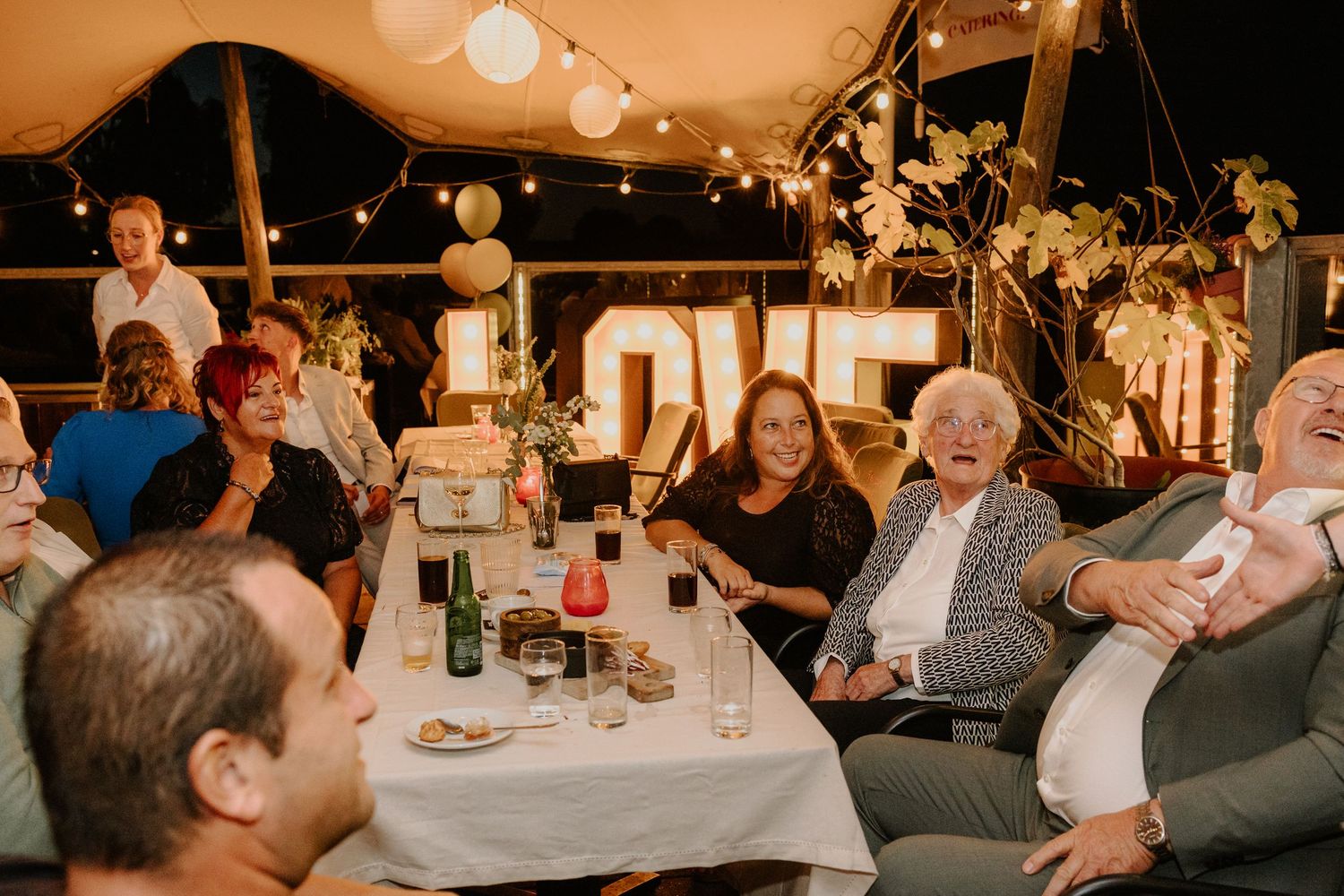 Bruiloftsgasten aan tafel tijdens het feest op een sfeervol verlichte trouwlocatie