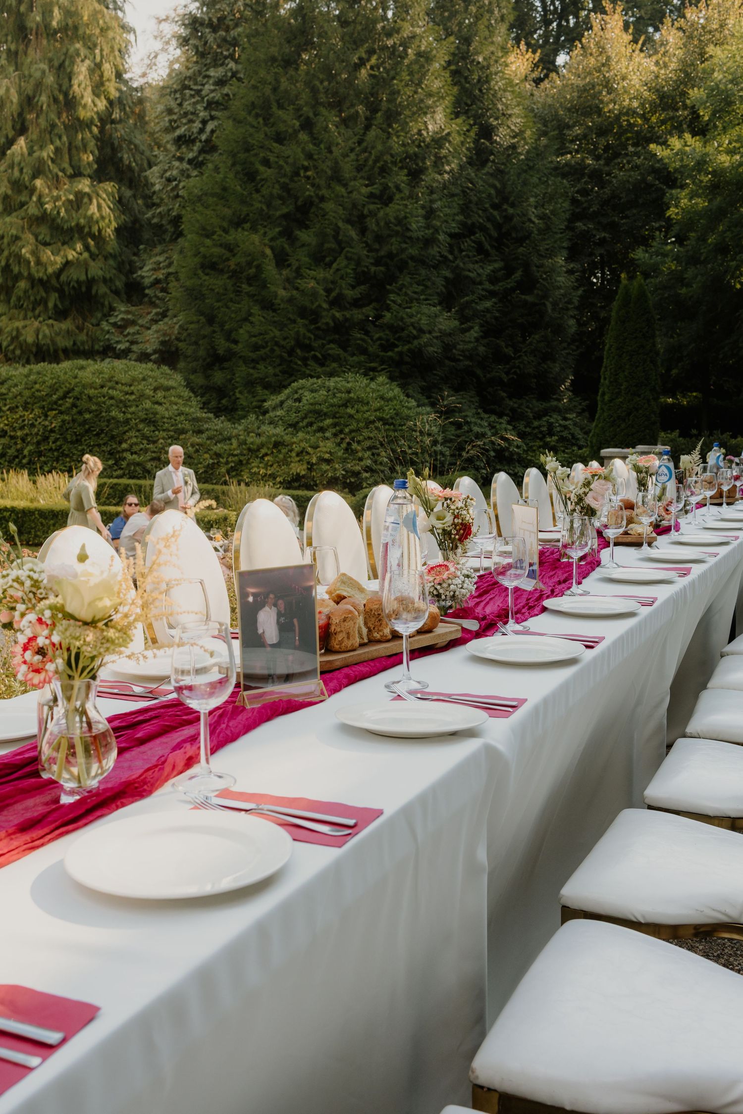 Gedekte lange dinertafel tussen het groen tijdens een buitenbruiloft