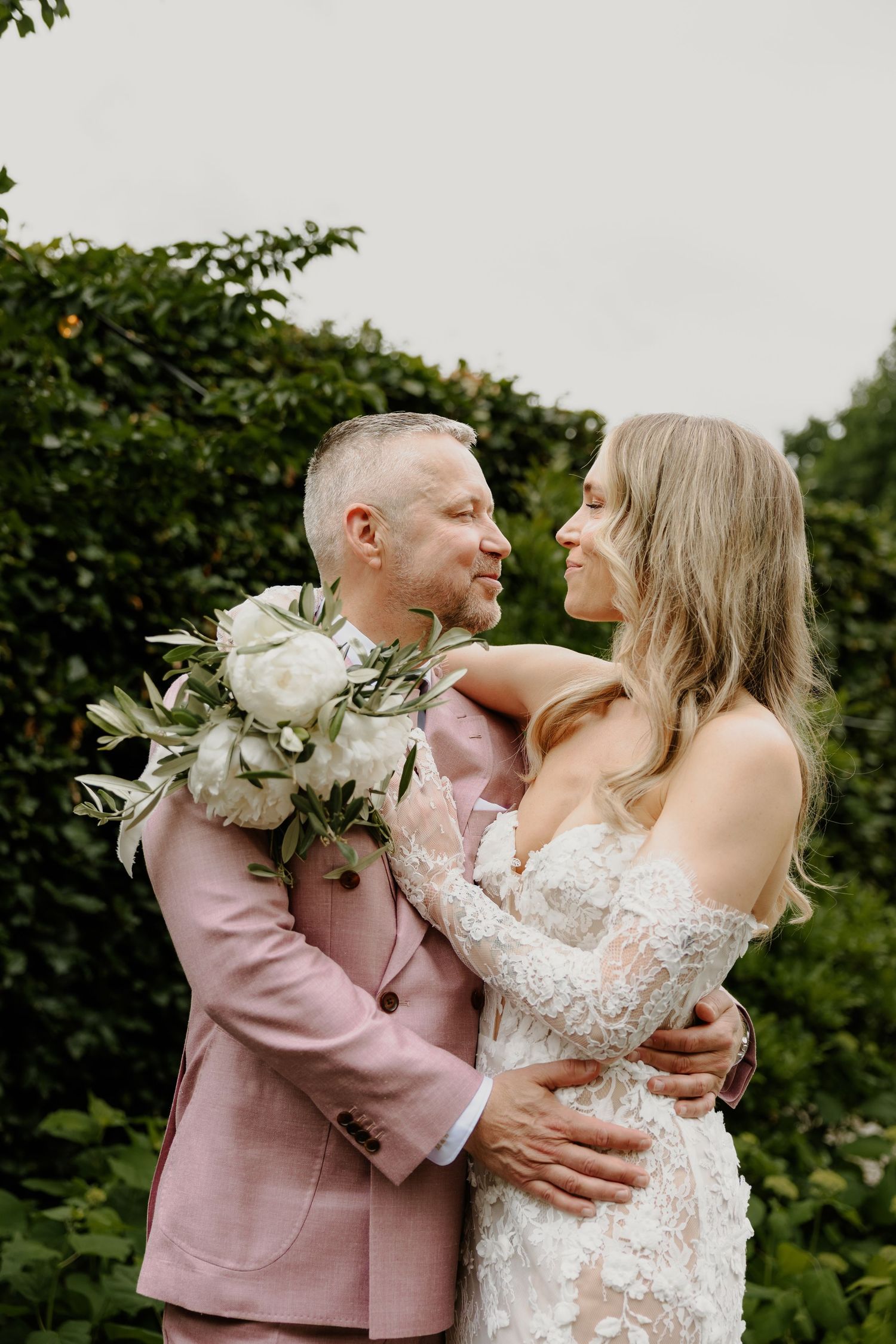 Bruidegom kijkt liefdevol naar zijn bruid terwijl zij hem omarmt met haar bruidsboeket