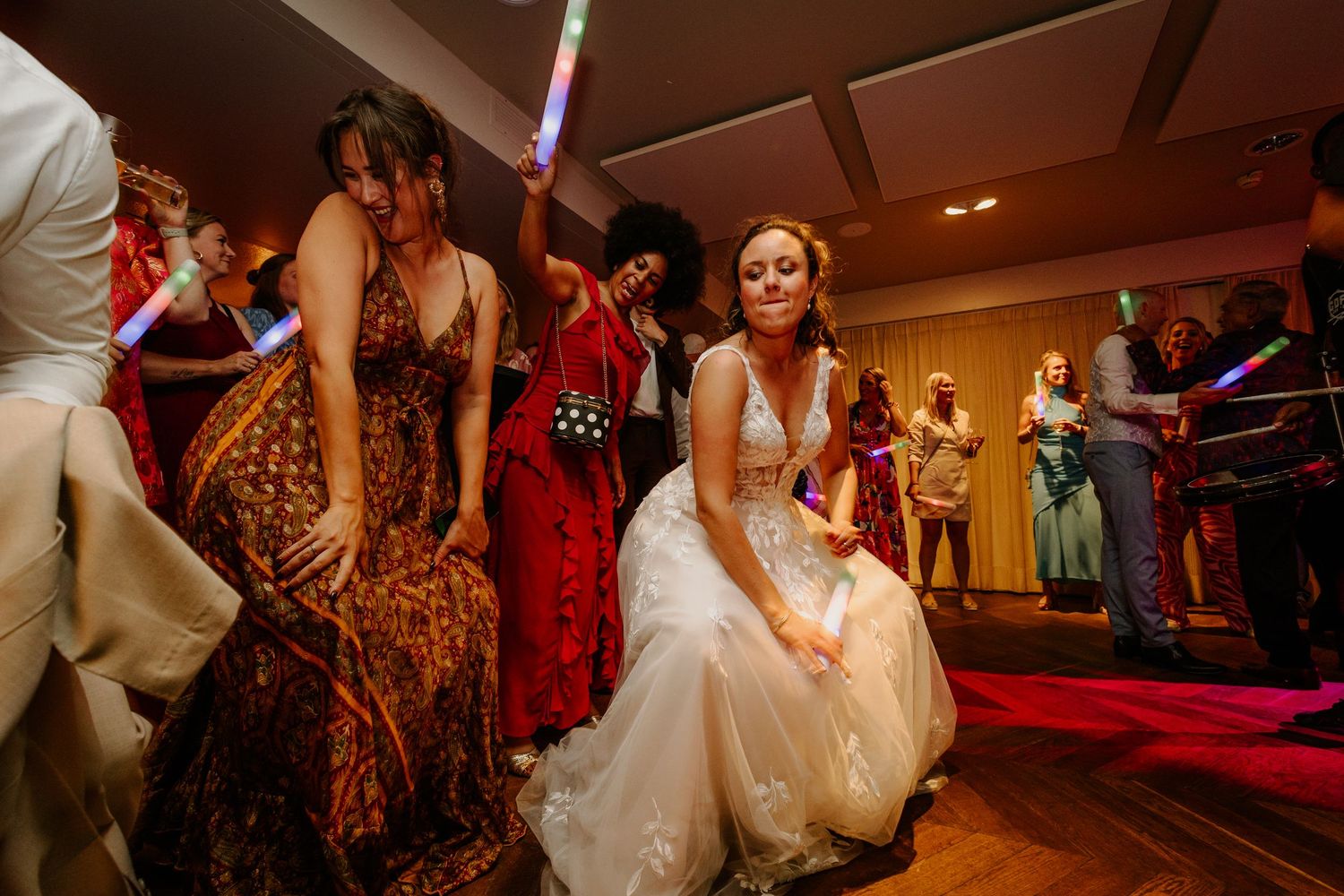 Bruid en gasten dansen samen tijdens een kleurrijk verlicht trouwfeest.