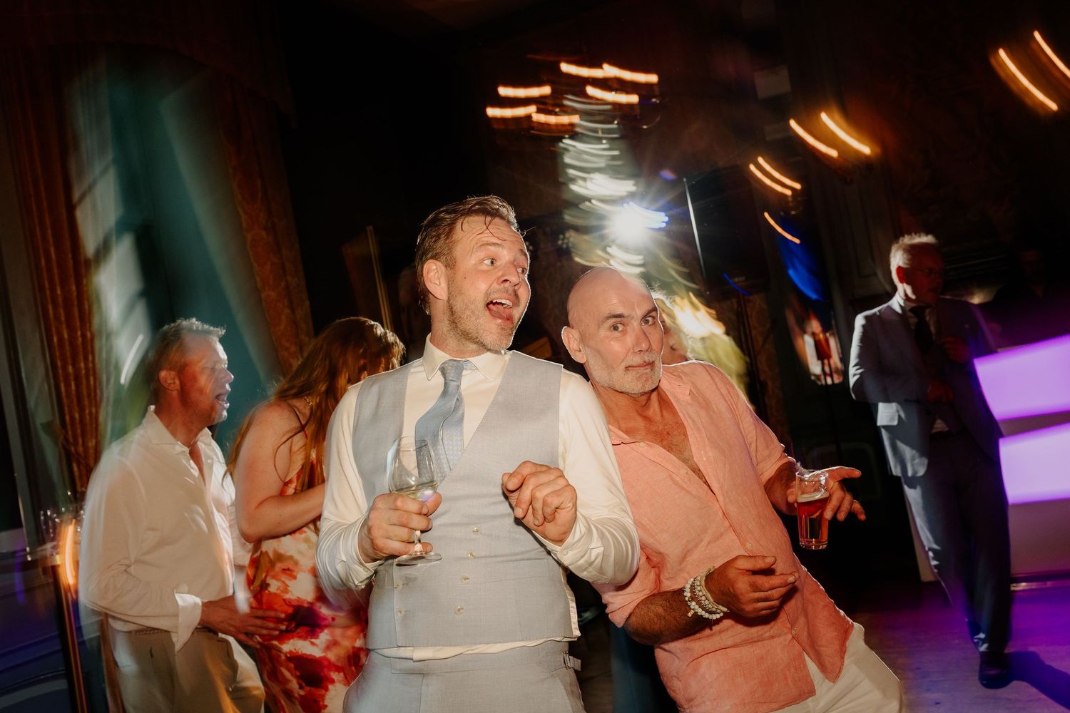 Twee mannen dansen lachend samen tijdens een kleurrijk trouwfeest