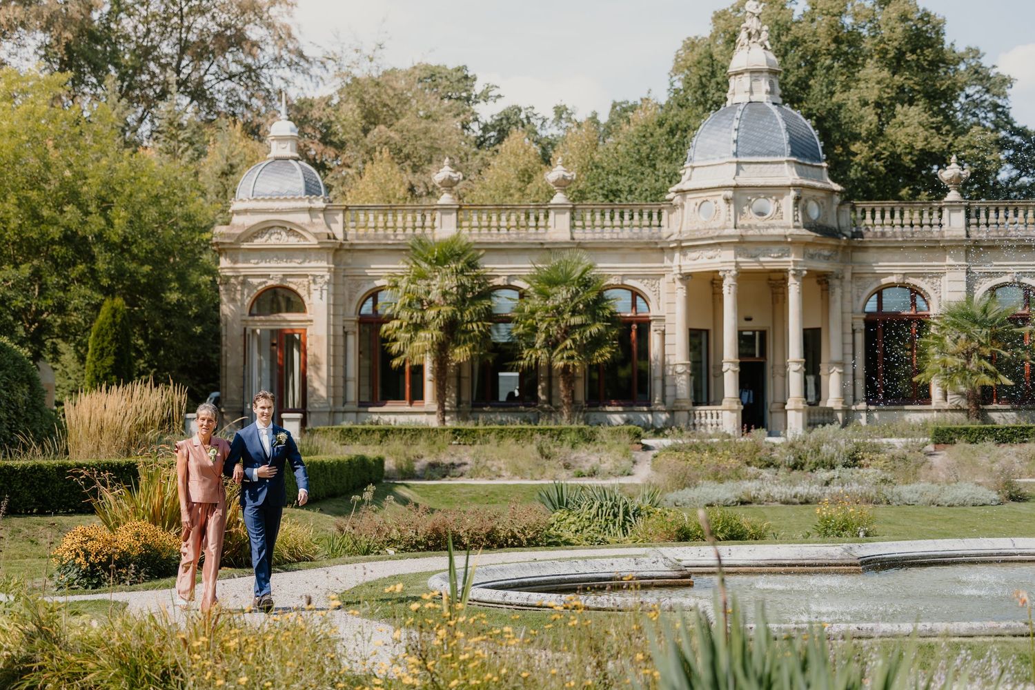 Bruidegom wordt door zijn moeder naar de ceremonie begeleid bij Oranjerie Hydepark