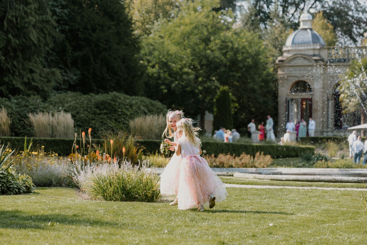 bruidsmeisjes rennen giegelend door de tuin met een klassiek paviljoen op de achtergrond