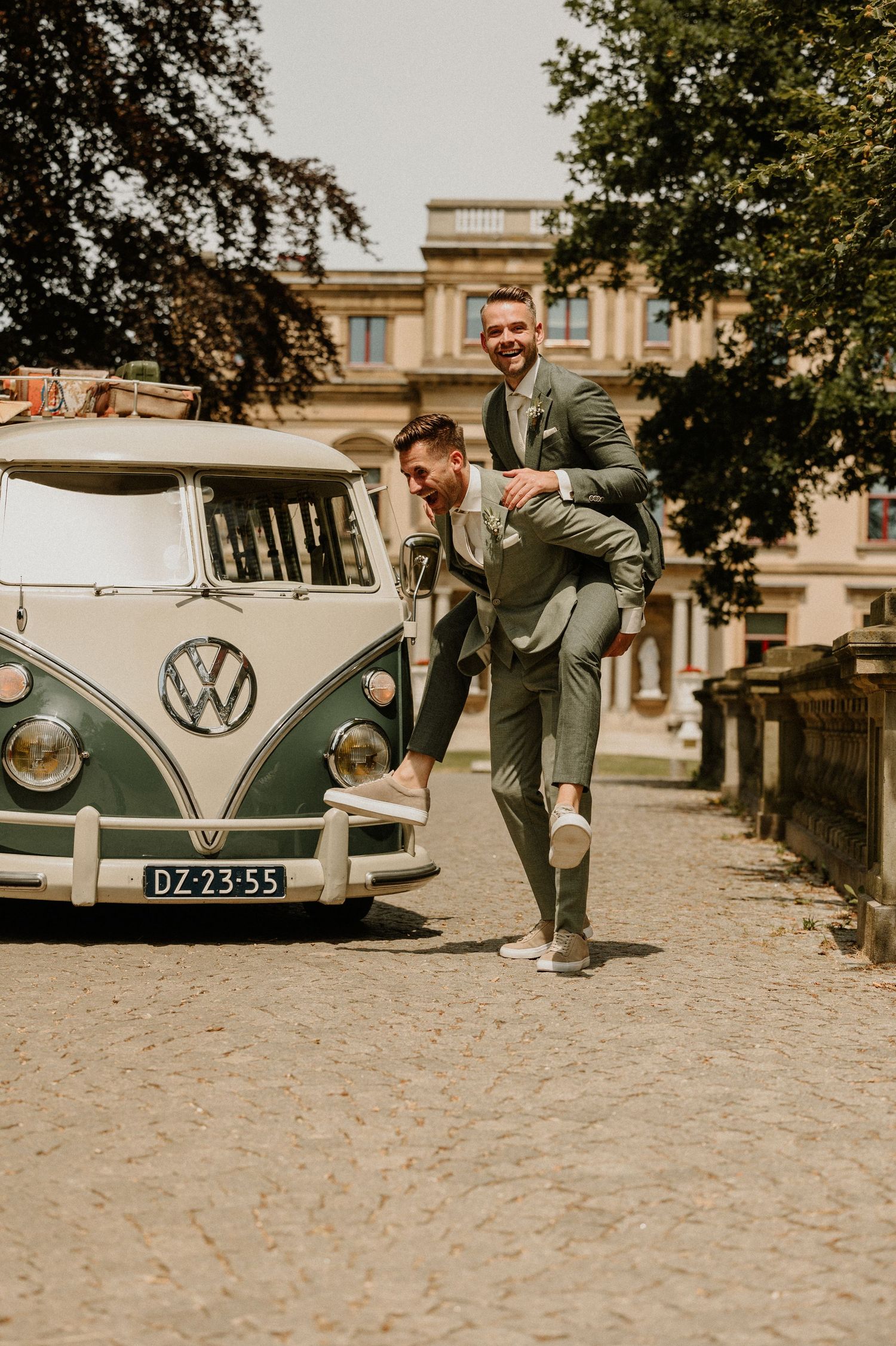 Bruidegom heeft zijn echtgenoot op zijn rug bij een vintage Volkswagenbus op zijn trouwdag