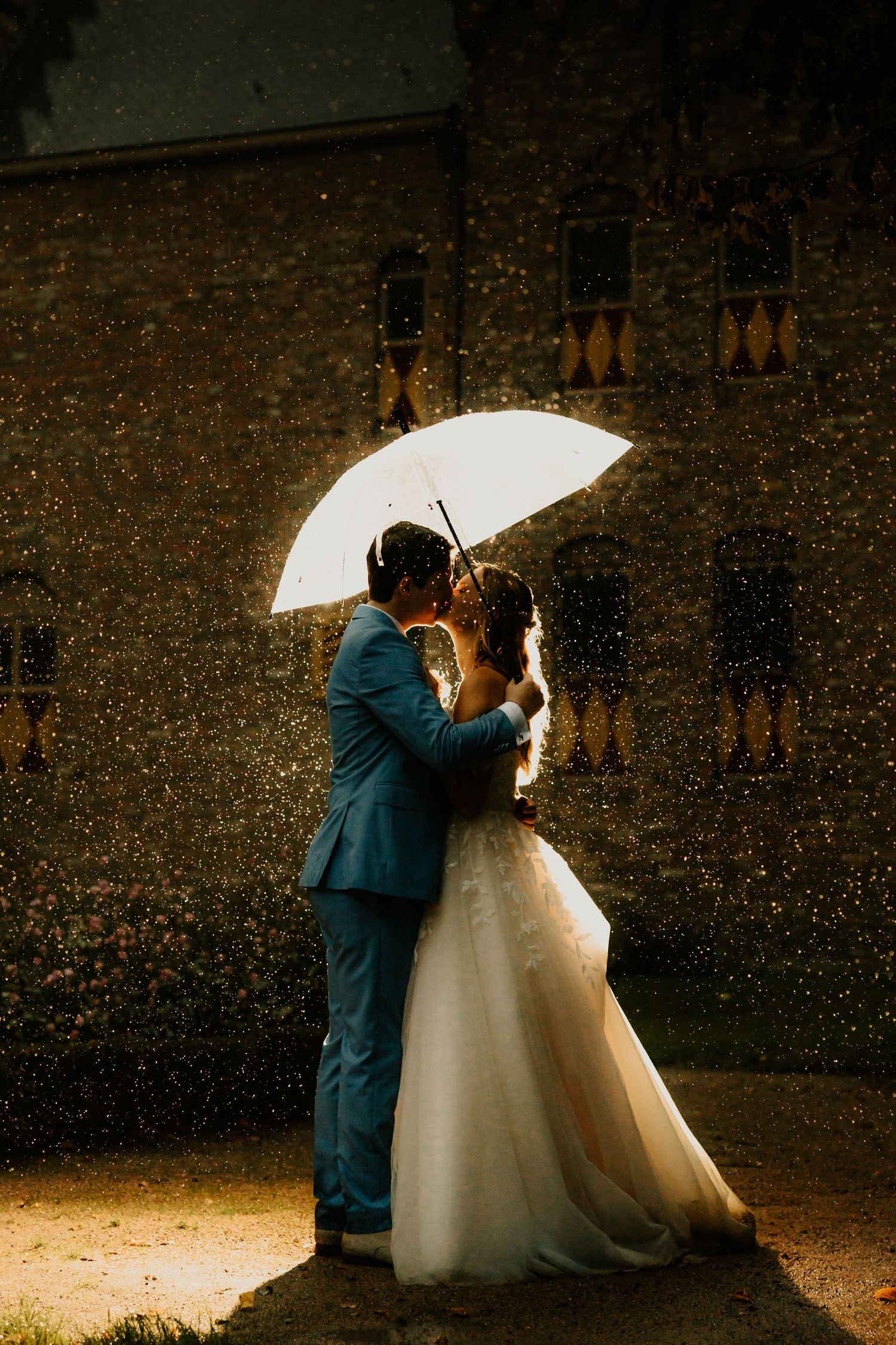 Bruidspaar staat in de regen onder een paraplu met een felle backlight